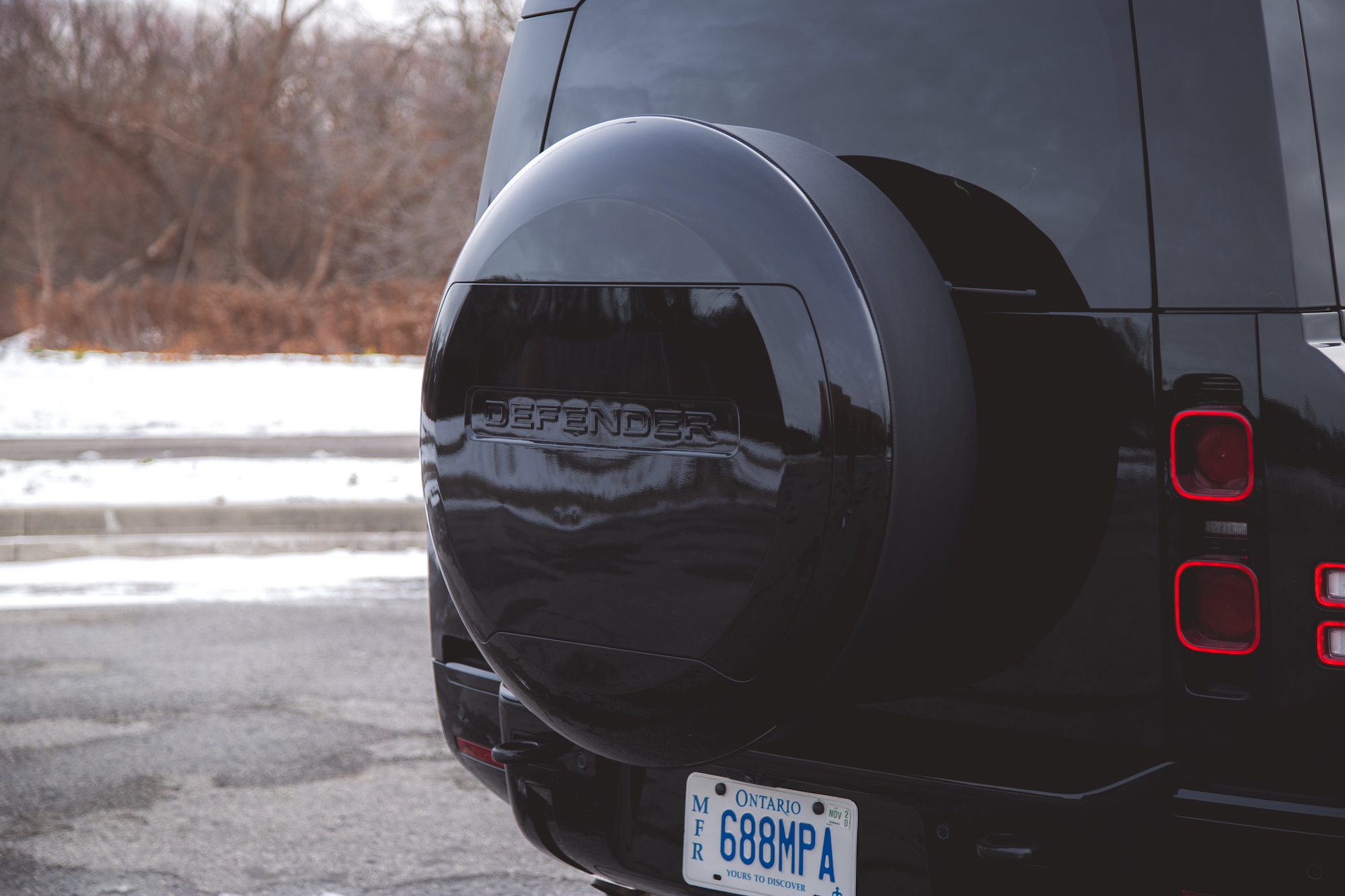 Rear view of a 2026 Land Rover Defender 130 in Santorini Black, showing the spare tire cover with 'DEFENDER' engraved, and Ontario license plate.