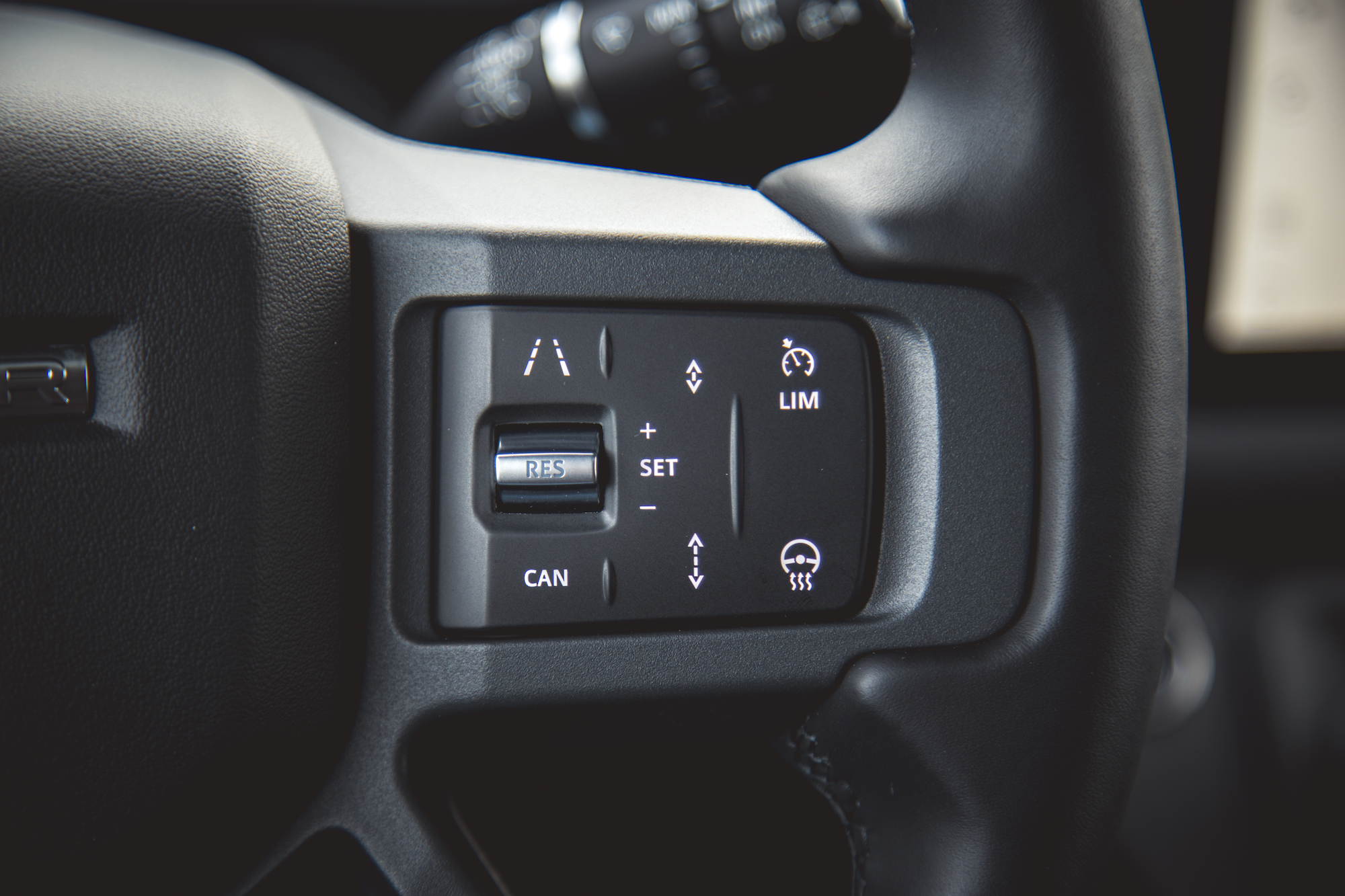 Close-up view of the steering wheel controls in a 2026 Land Rover Defender 130, featuring buttons for cruise control and lane assist.
