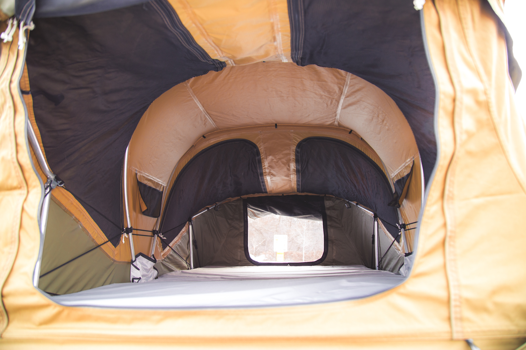 Interior view of a Thule Approach rooftop tent, featuring a spacious layout with a foam mattress, large zip windows, and integrated bug screens.