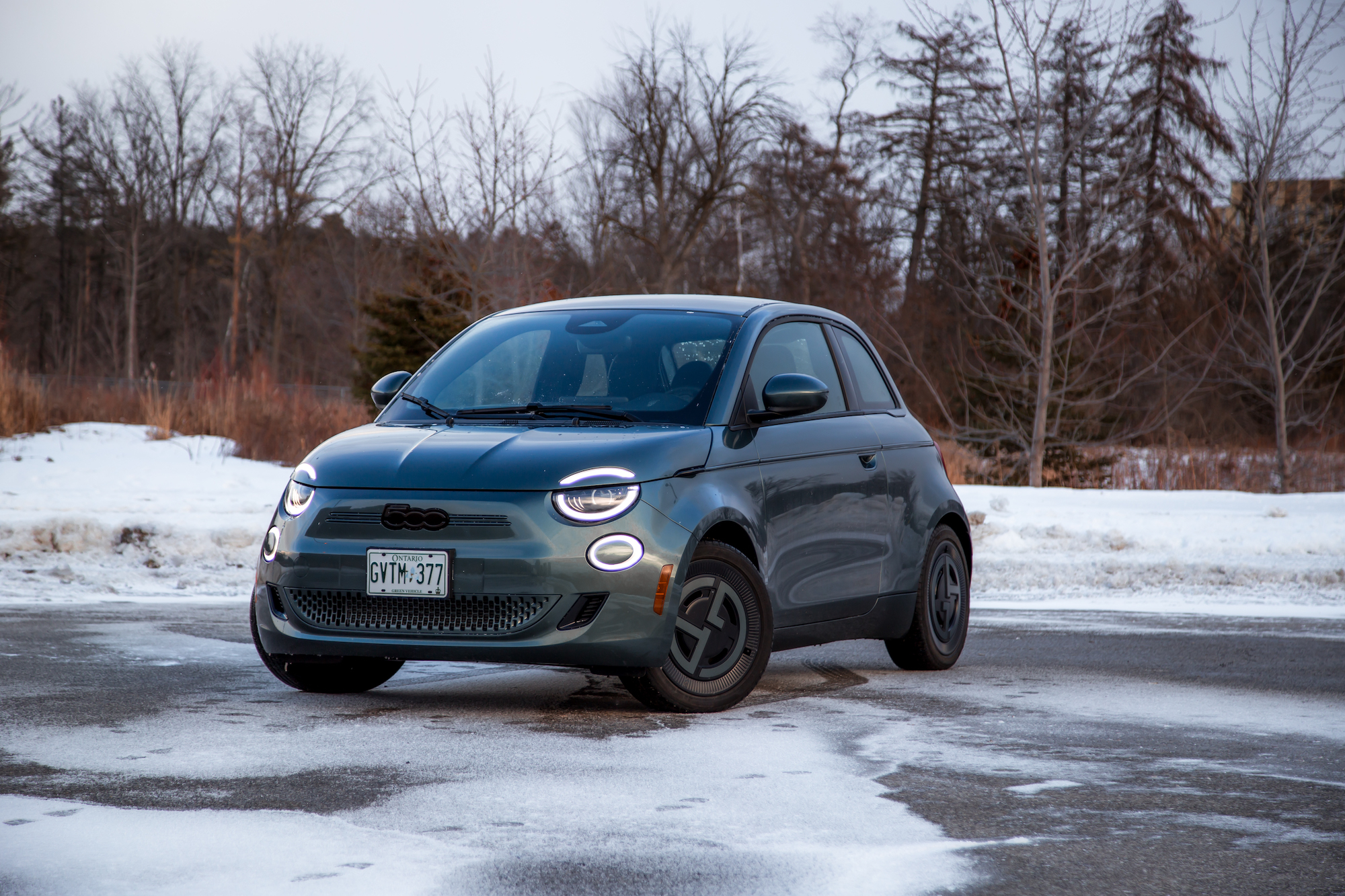 A compact electric car parked on a snowy road, featuring a sleek design with round headlights and a modern aesthetic.