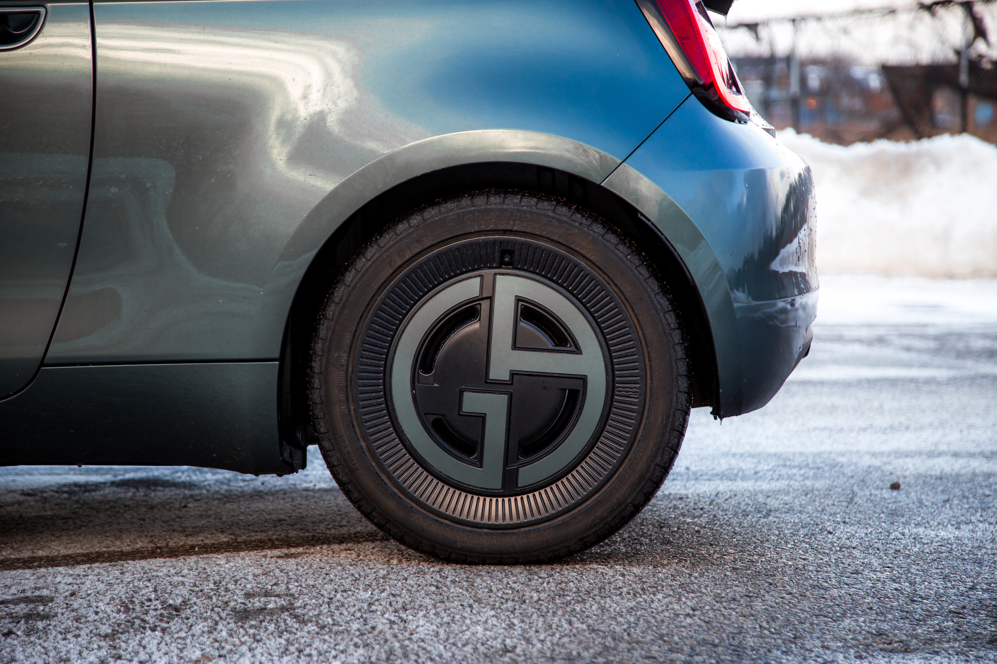 Close-up of a stylish car wheel with a unique design featuring a circular logo, mounted on the rear of a teal vehicle.