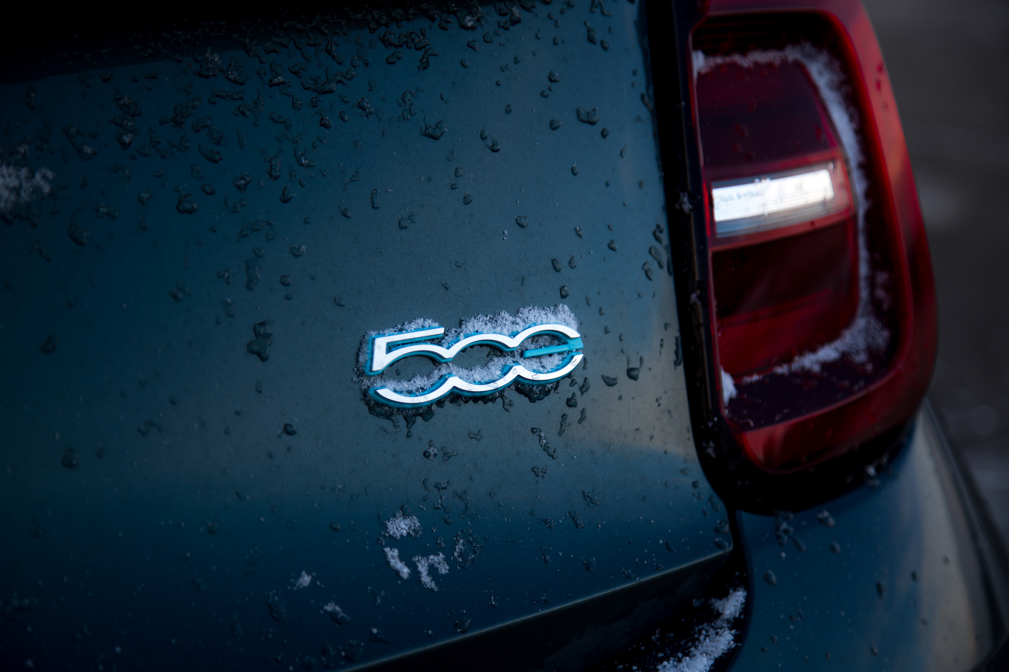 Close-up of a car's rear emblem featuring the number '500', with a snowy and wet surface.