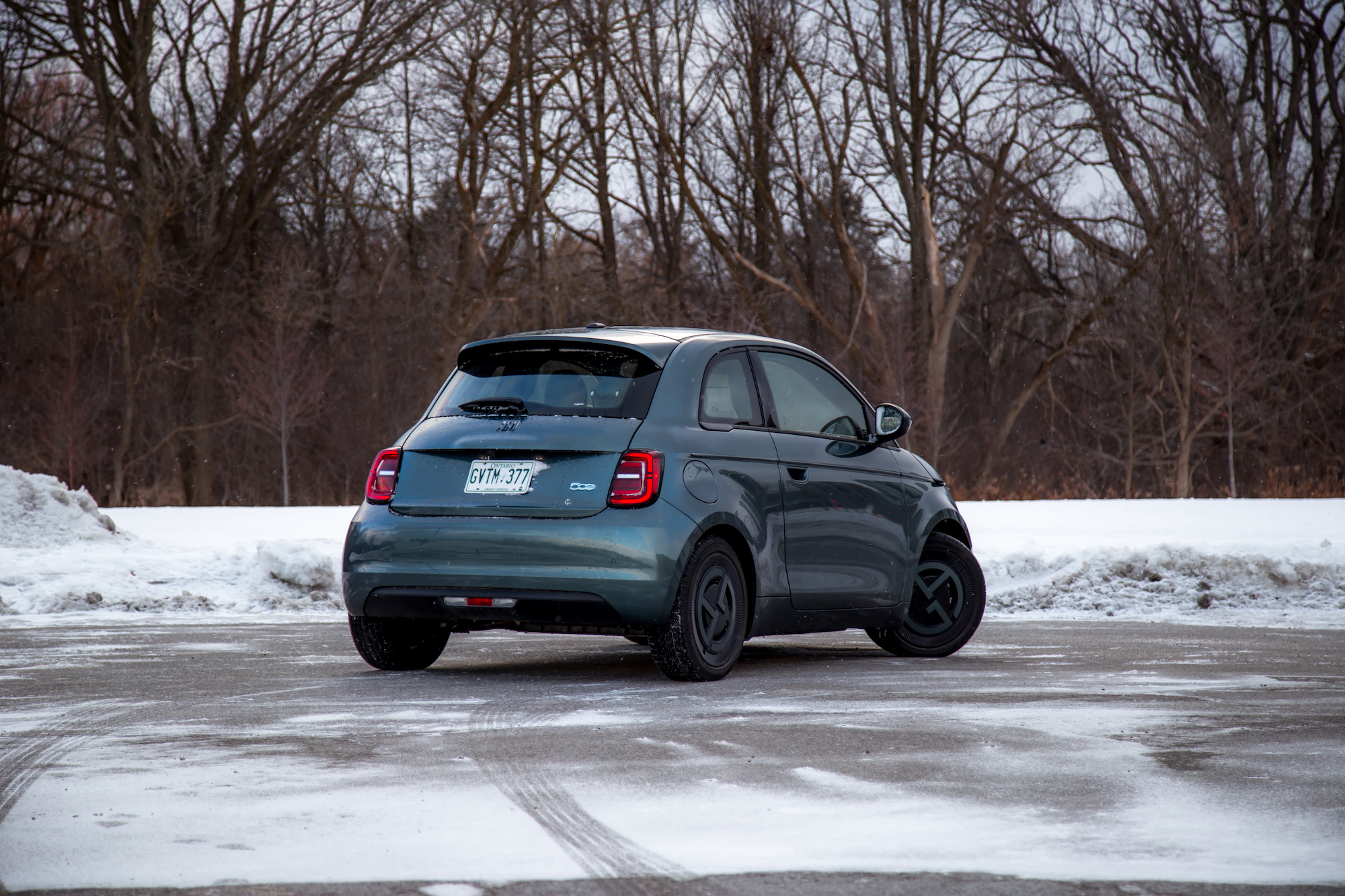 A compact car parked on a snowy surface with trees in the background, viewed from the rear at a slight angle.