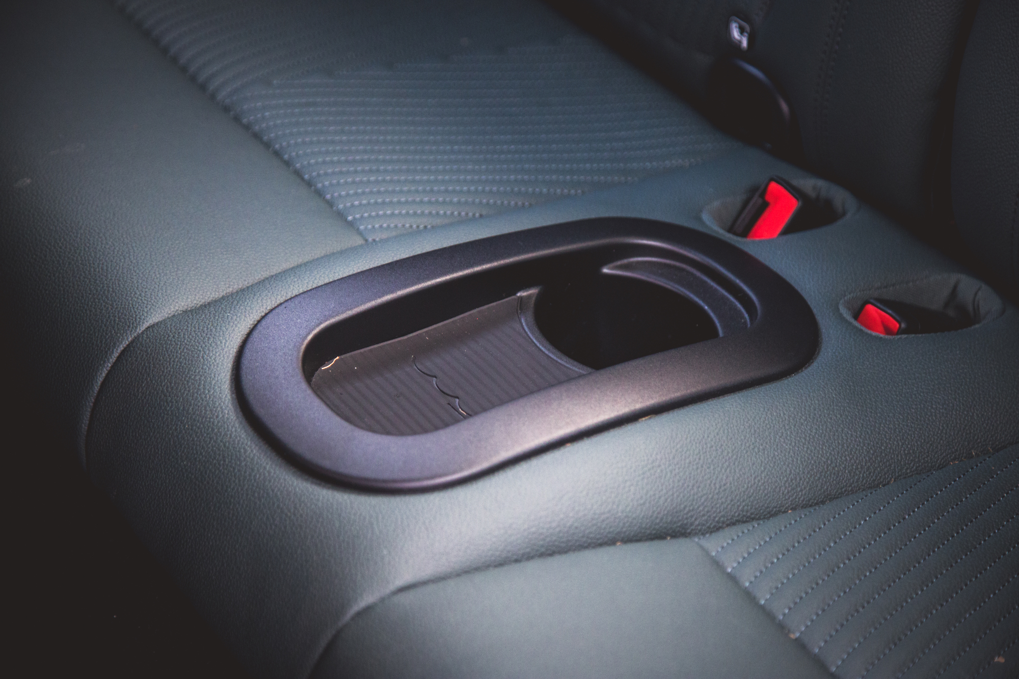 Close-up of a car seat armrest with a cup holder, showcasing leather upholstery and red seatbelt clips.