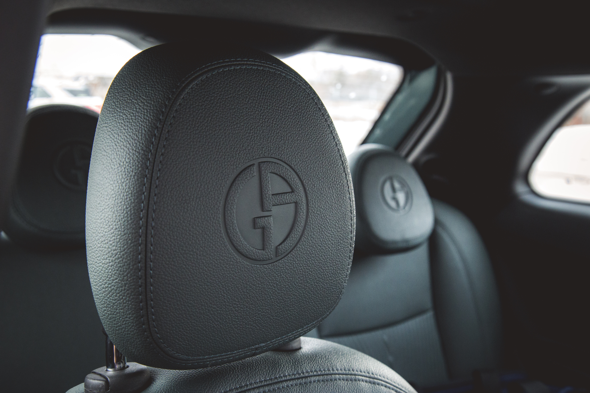 Close-up of a car seat headrest featuring a logo embossed on the leather material.