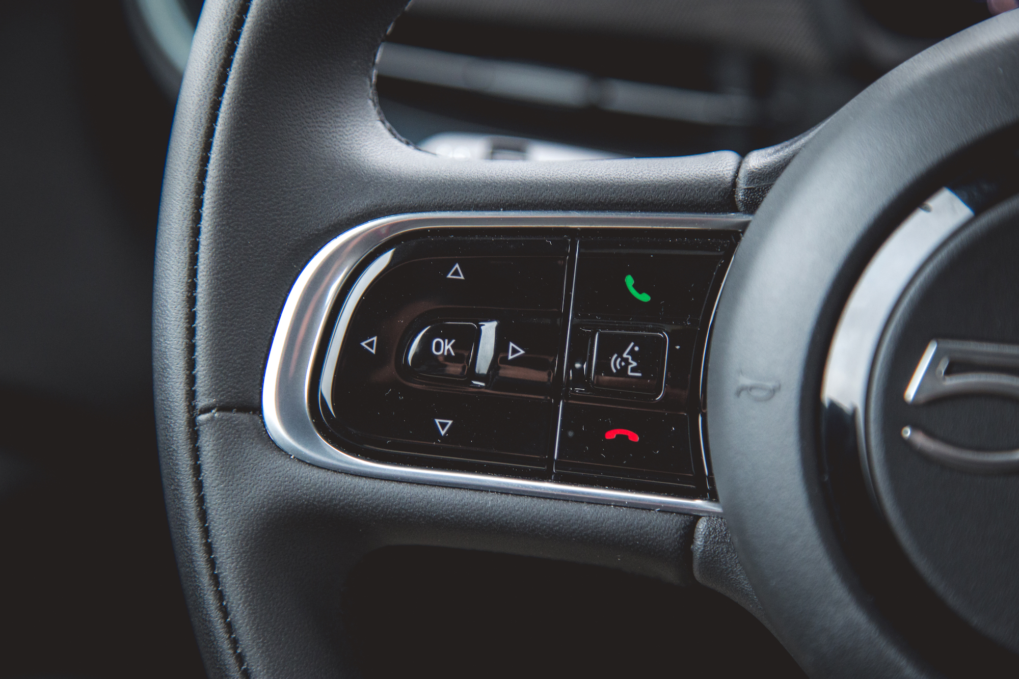 Close-up of a car steering wheel control panel featuring buttons for navigation, phone calls, and audio settings.