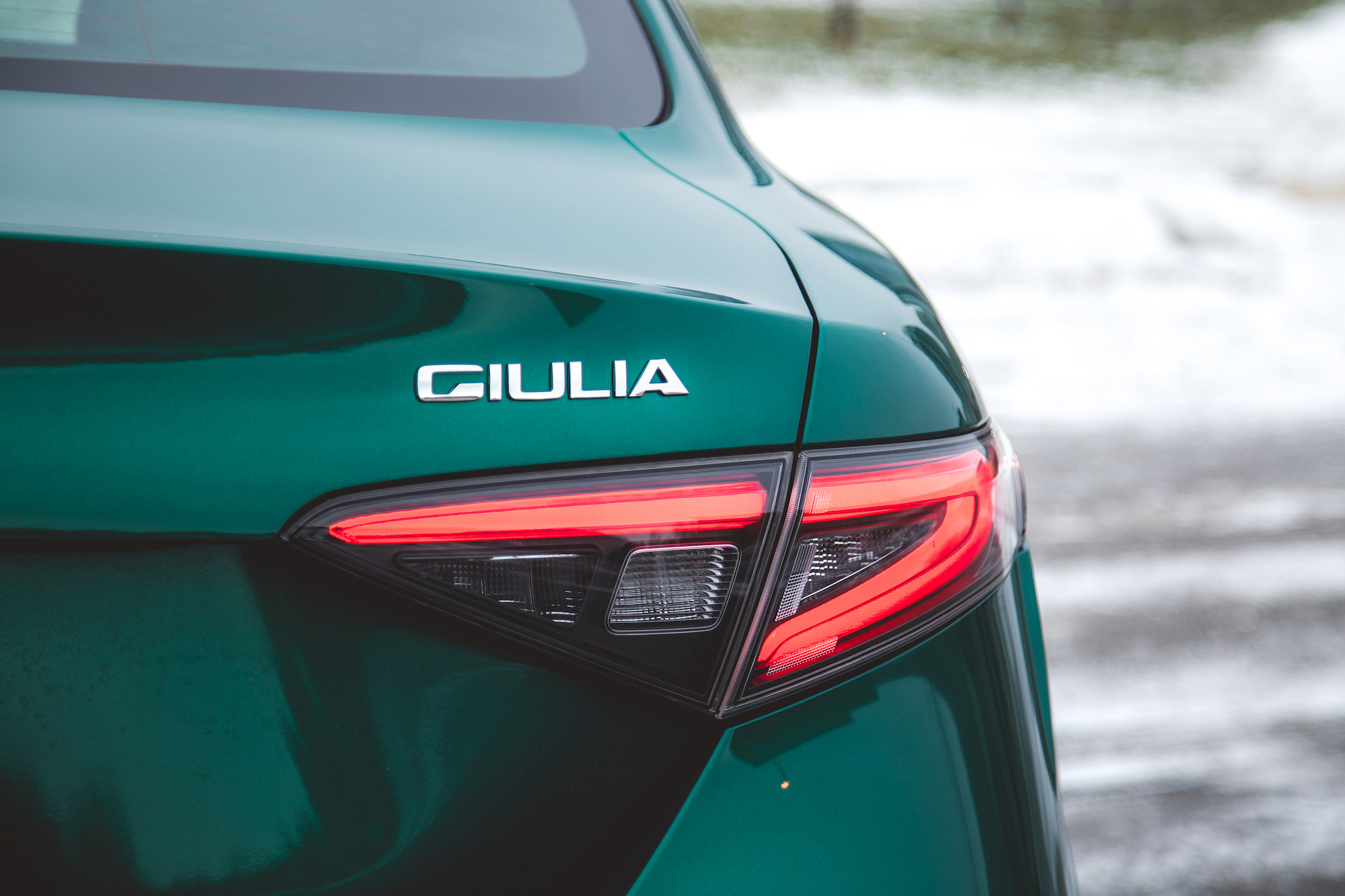 Primer plano de la parte trasera de un Alfa Romeo Giulia verde, con el logotipo de la marca y las luces traseras.