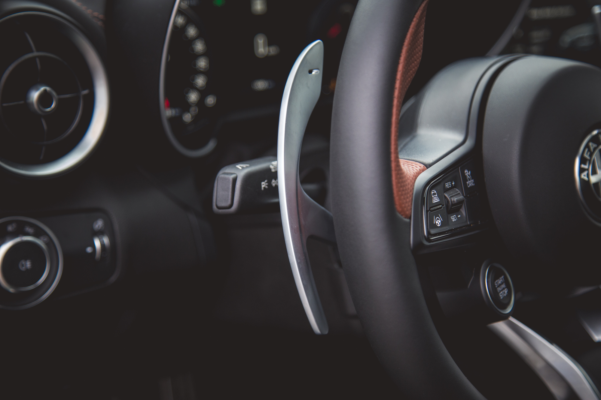 Primer plano del volante de un automóvil con levas de cambio, botones de control y un botón de arranque y parada del motor.