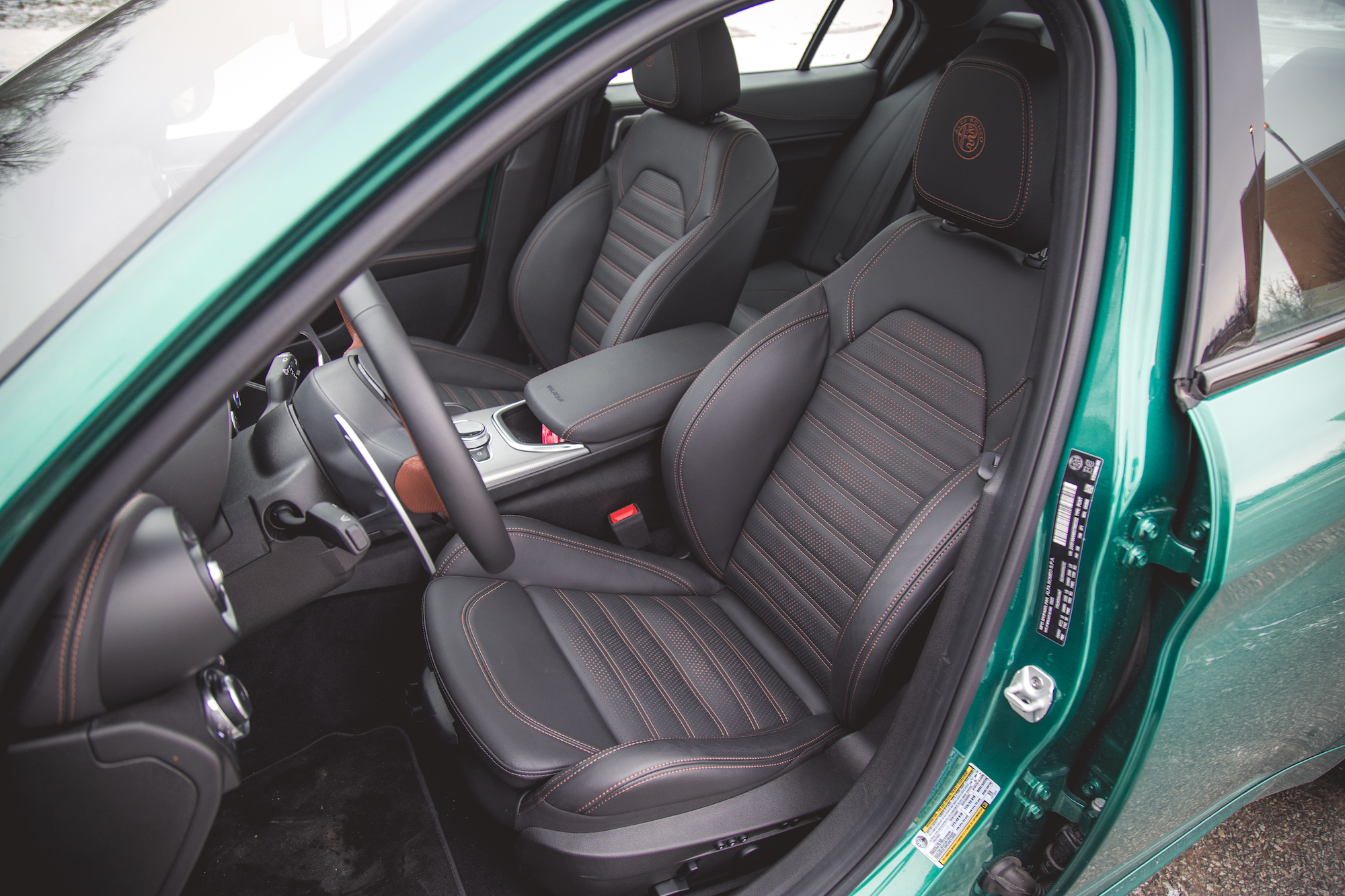 Vista interior de un automóvil con dos asientos delanteros deportivos con tapizado de cuero negro y costuras en naranja, volante y elementos modernos en el tablero.