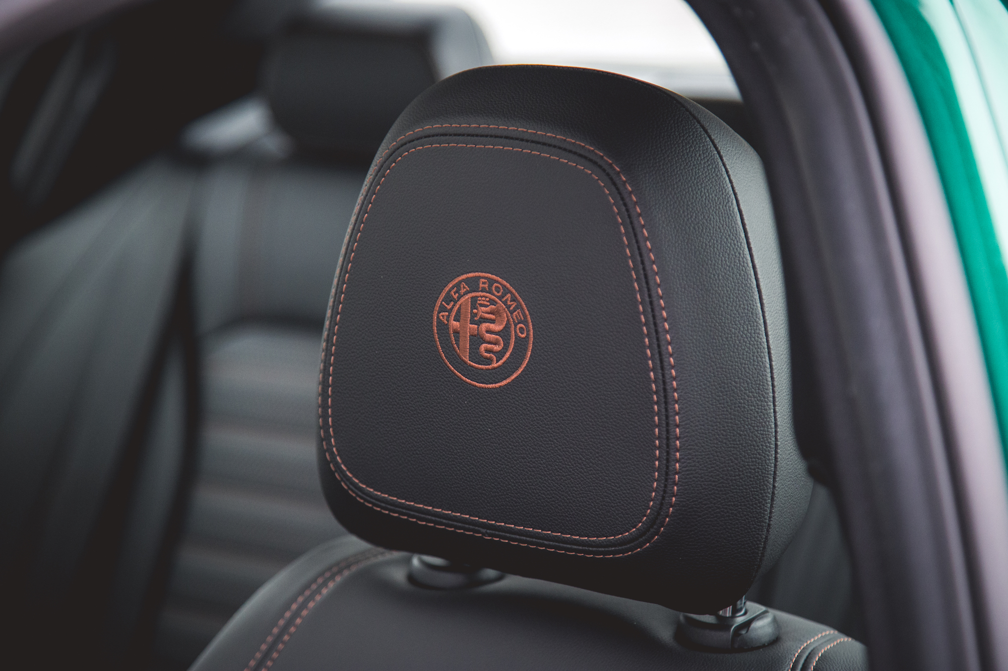 Primer plano del reposacabezas de un automóvil Alfa Romeo con logotipo y costuras en contraste.