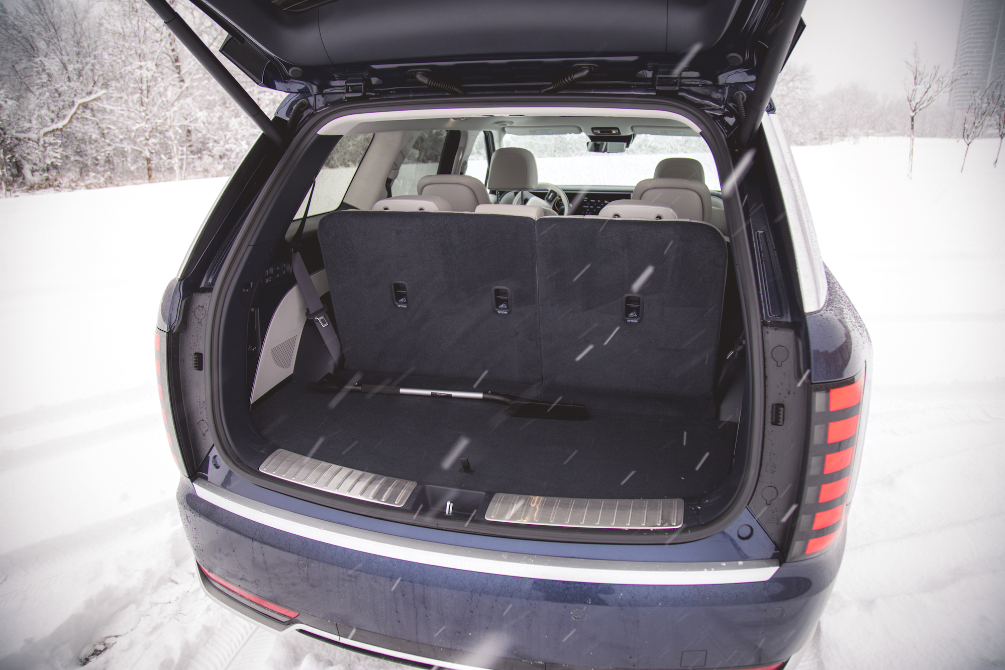Vista trasera del área de carga de un SUV con el maletero abierto, que muestra un interior espacioso y asientos traseros abatidos, rodeado de nieve recién caída.