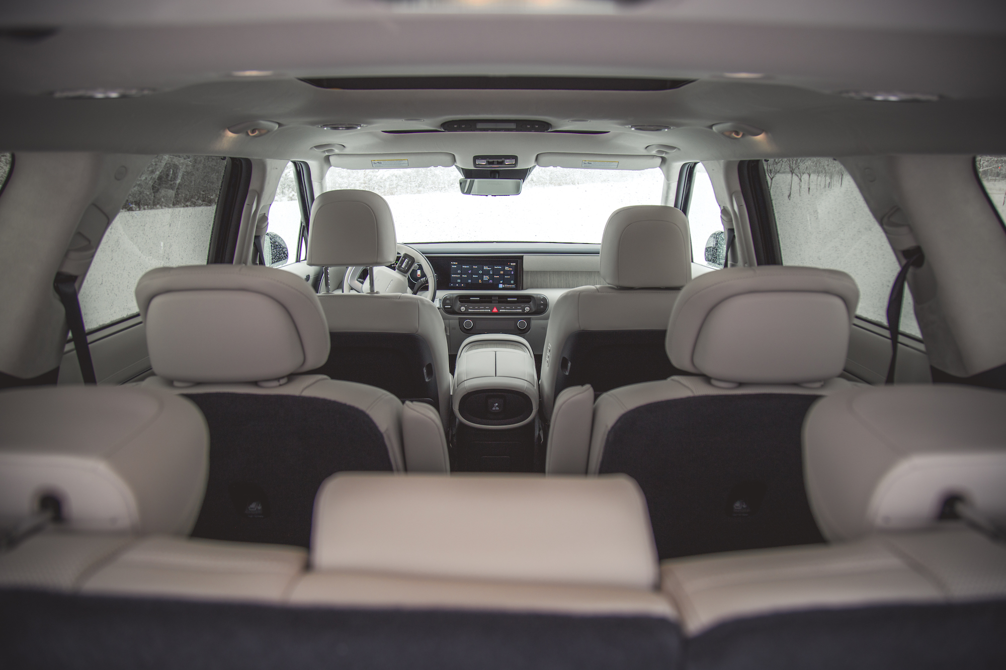 Vista interior de un SUV moderno que muestra la zona de asientos traseros, el tablero y la consola delantera, con lluvia en las ventanas.