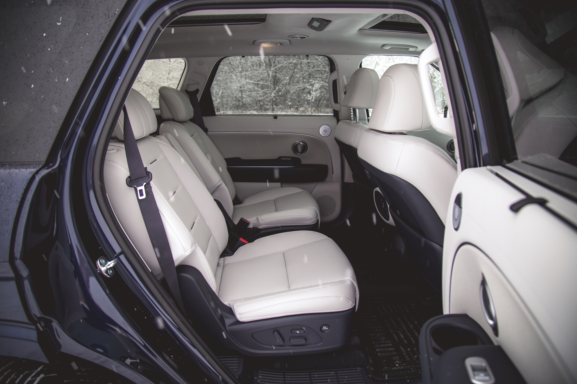 Vista interior de un vehículo que muestra la zona de asientos trasera con asientos de cuero beige y cinturones de seguridad.