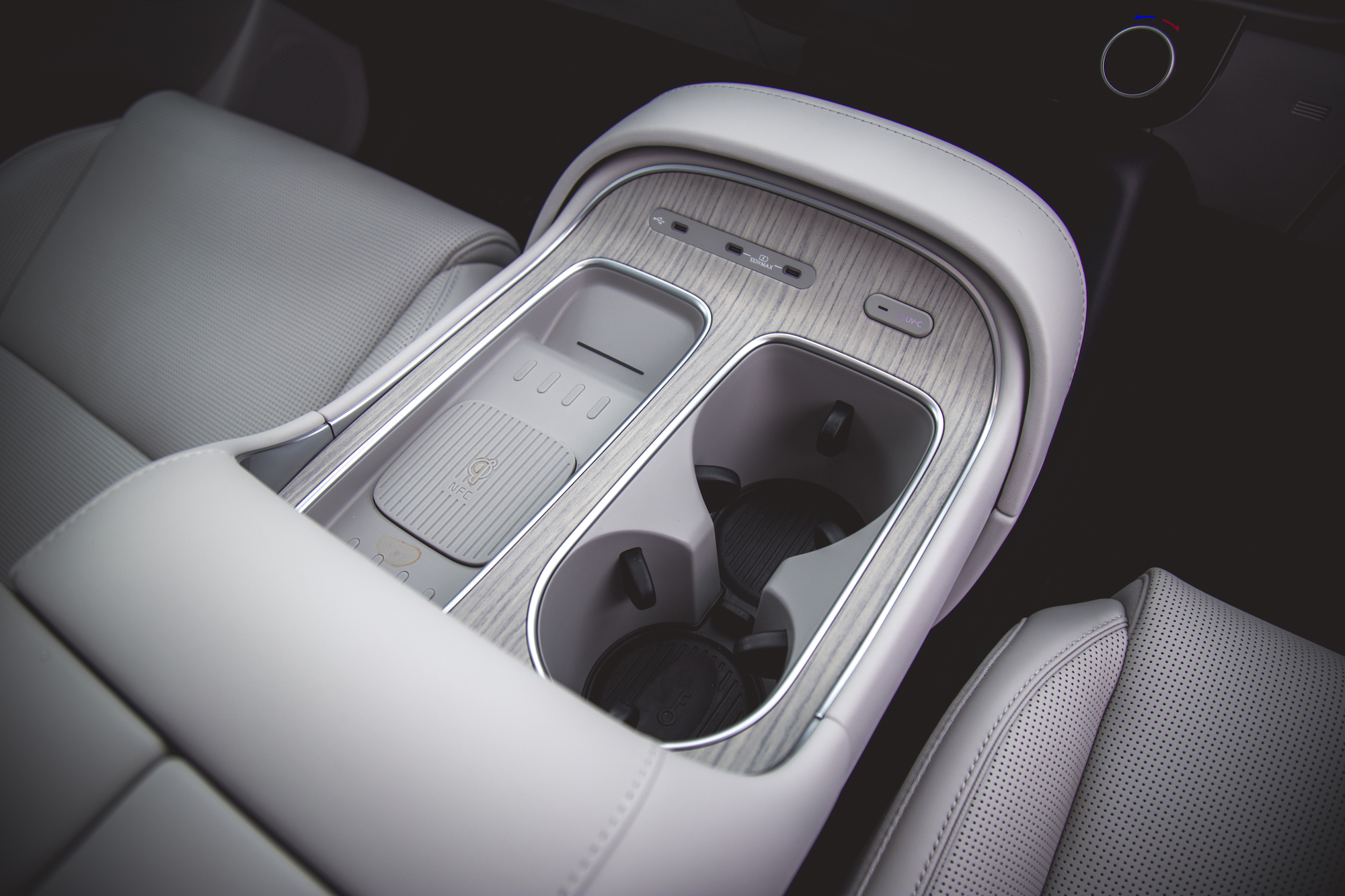 Una vista en primer plano de la consola central de un automóvil moderno con dos portavasos, un panel de control con botones y un diseño elegante con acabado de vetas de madera.