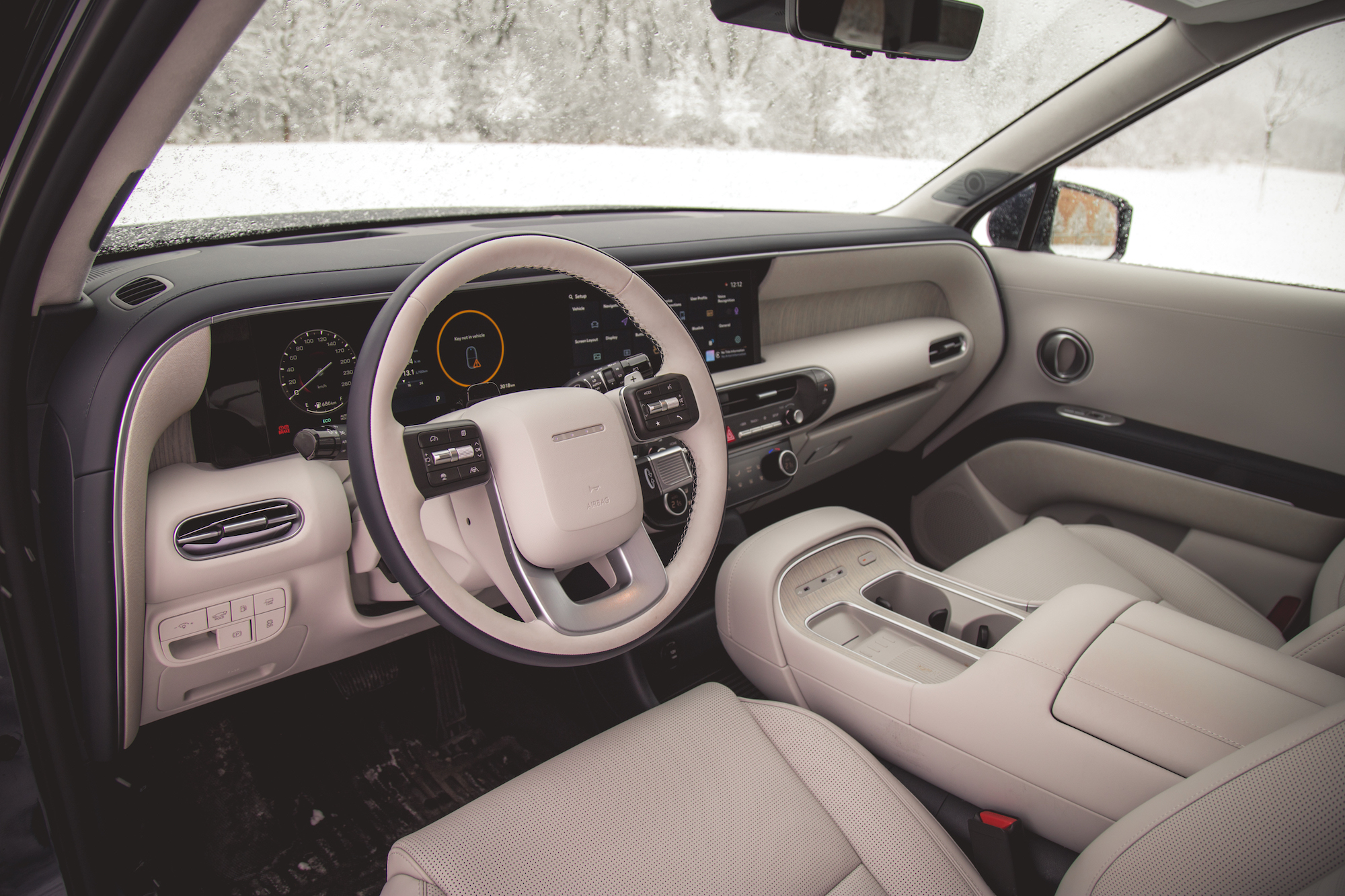 Vista interior de un automóvil moderno con volante blanco, pantallas avanzadas en el tablero y tapicería de colores claros.