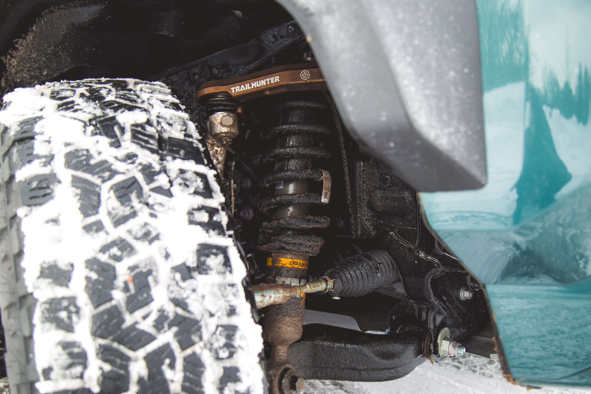 Vista cercana del sistema de suspensión de un camión y un neumático cubierto de nieve, destacando un componente de TRAILHUNTER.