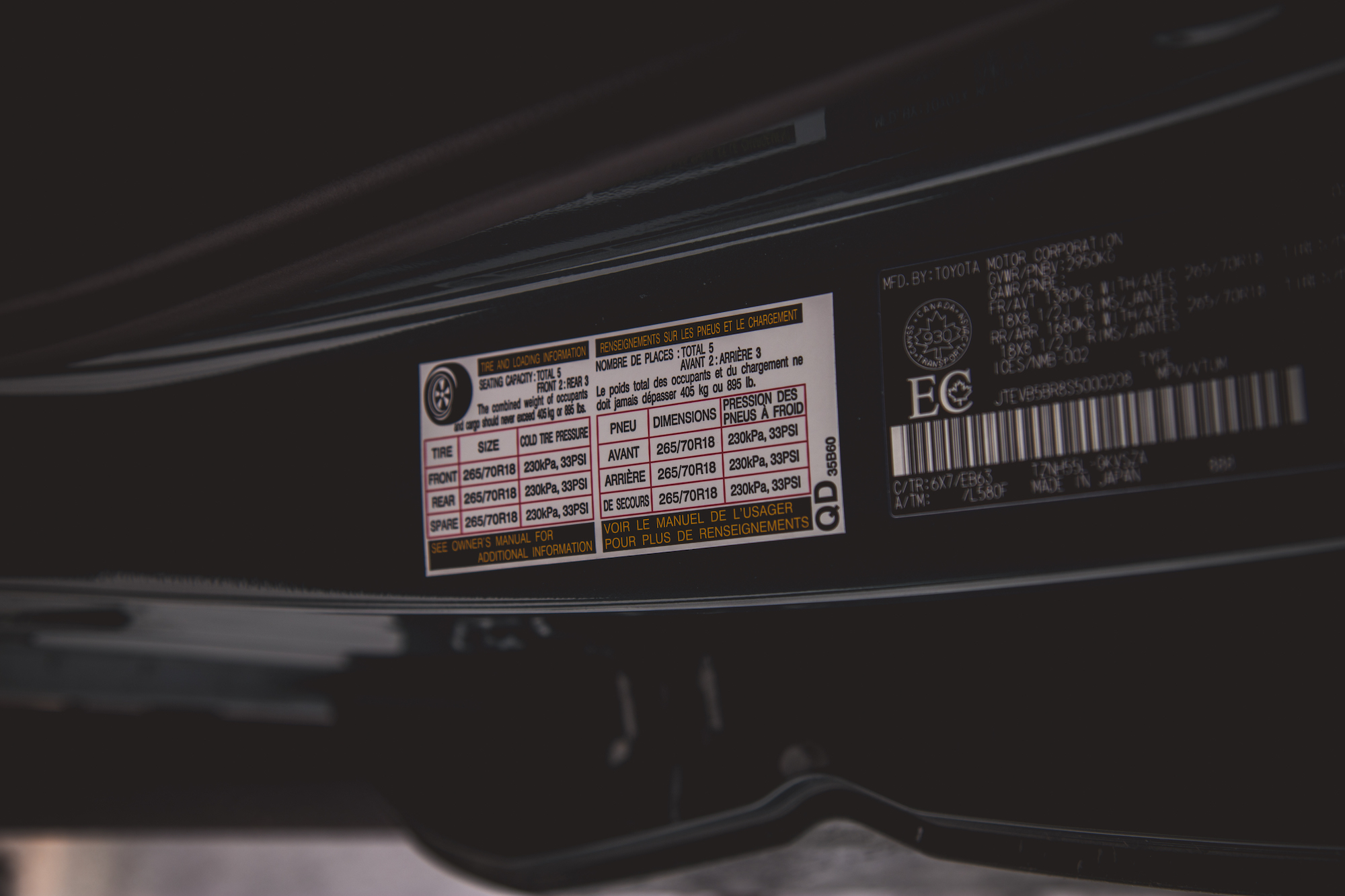 Primer plano de la llanta de un vehículo y una etiqueta de información de carga que muestra el tamaño de la llanta, las recomendaciones de presión y la capacidad de asientos.