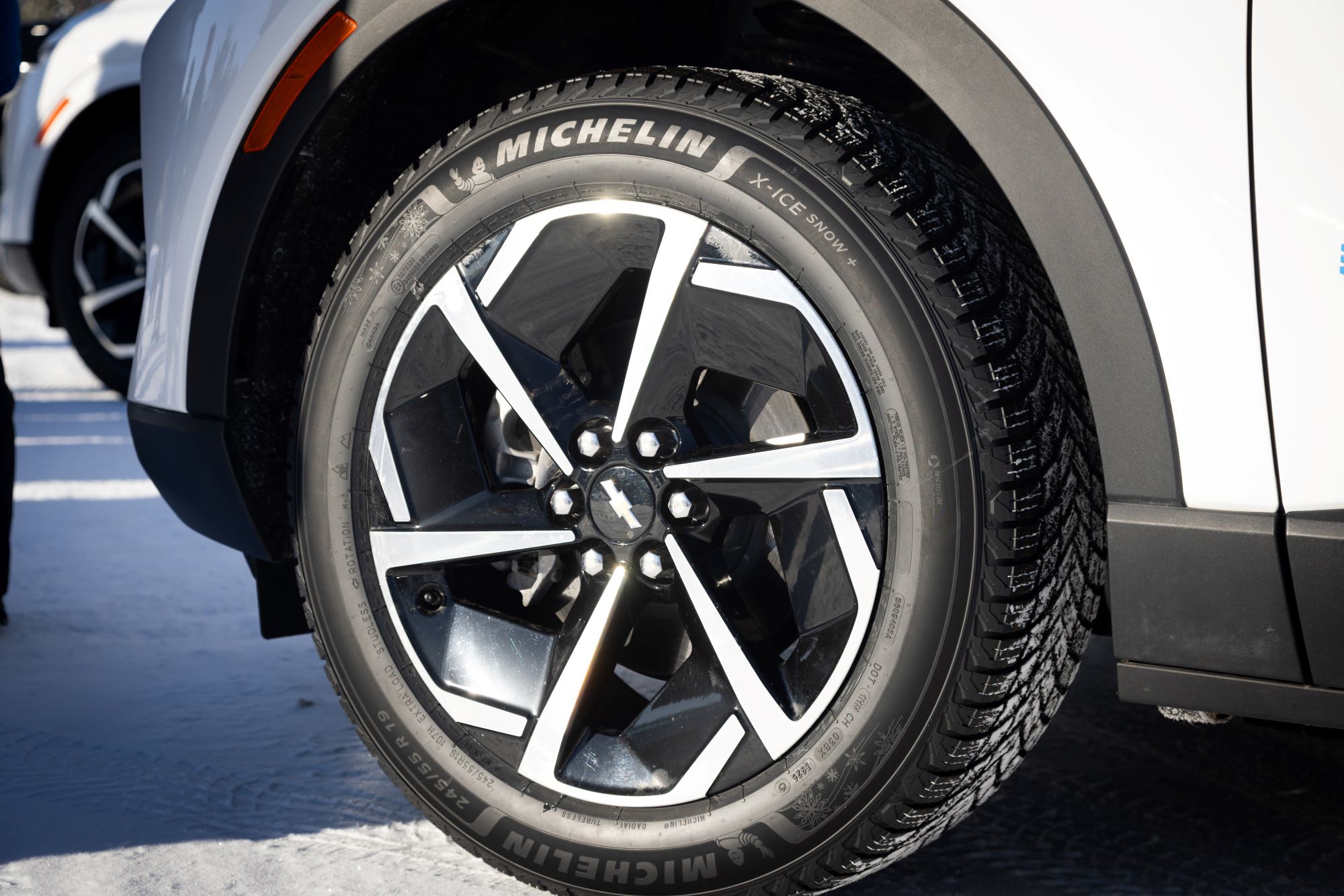 Close-up of a car wheel featuring a shiny multi-spoke alloy rim and a Michelin X-Ice Snow tire on a snowy surface.
