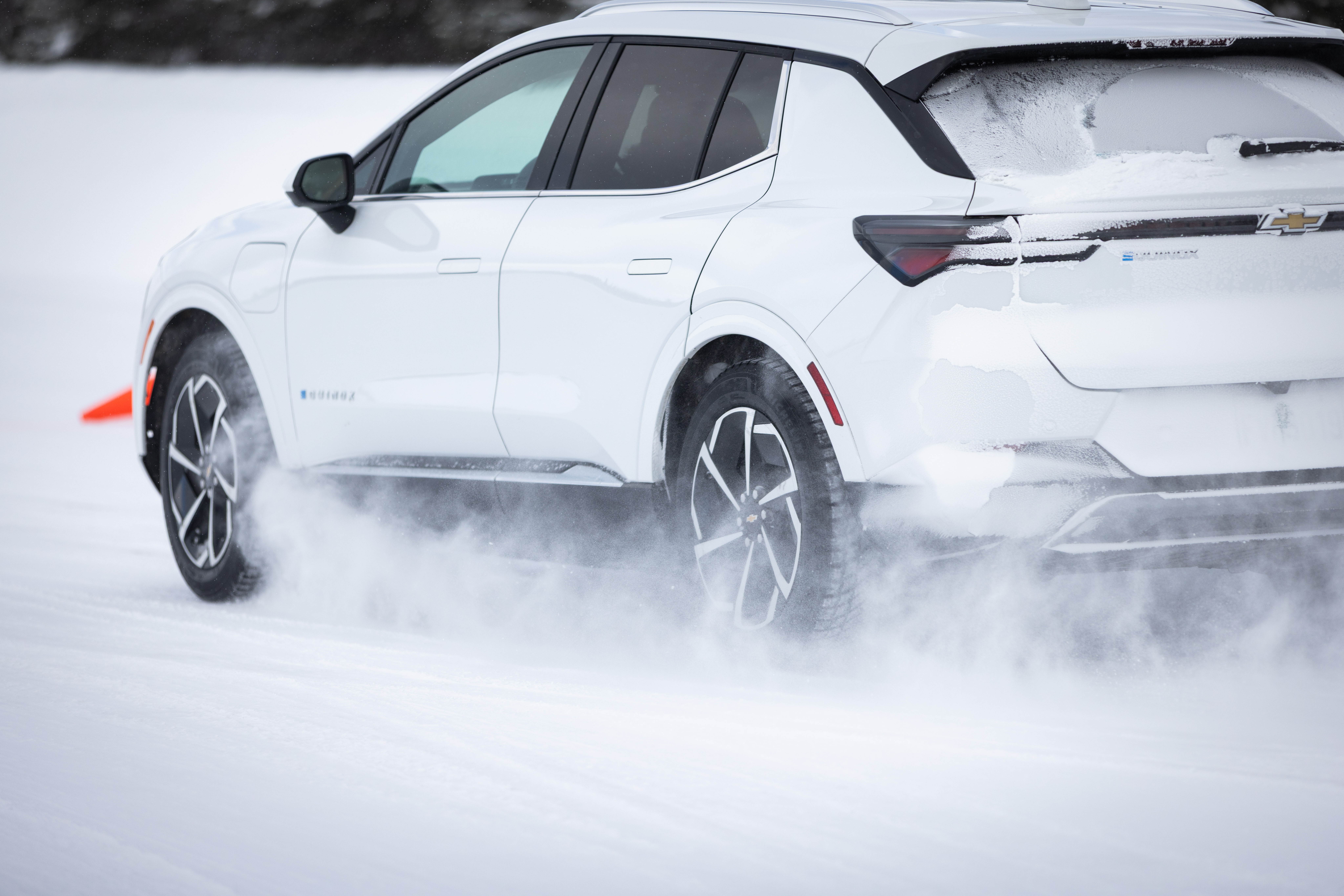 A white SUV driving on a snowy surface, with snow being kicked up by the tires.