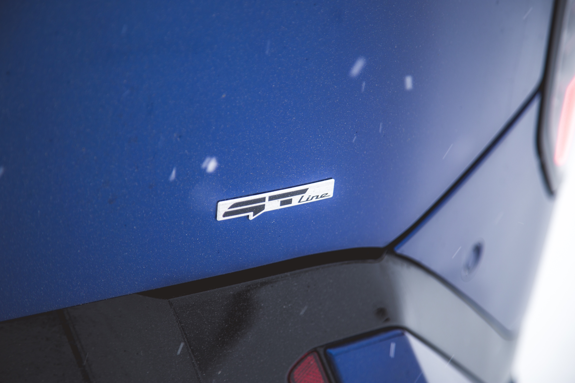 Primer plano de una insignia GT Line en un vehículo azul, con copos de nieve visibles en el aire.