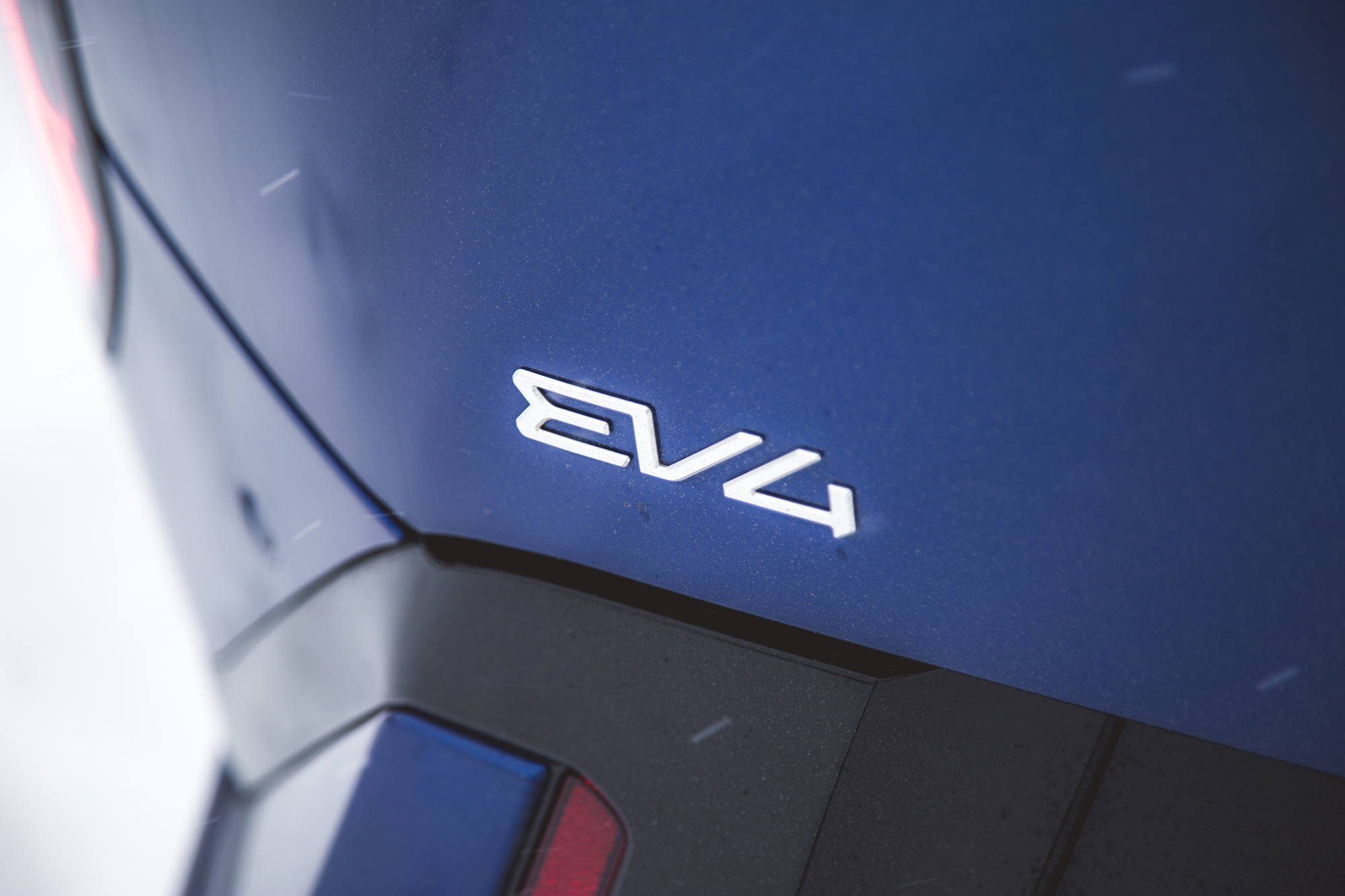 Primer plano de la insignia trasera de un automóvil que muestra el emblema 'EV4' sobre una superficie azul.