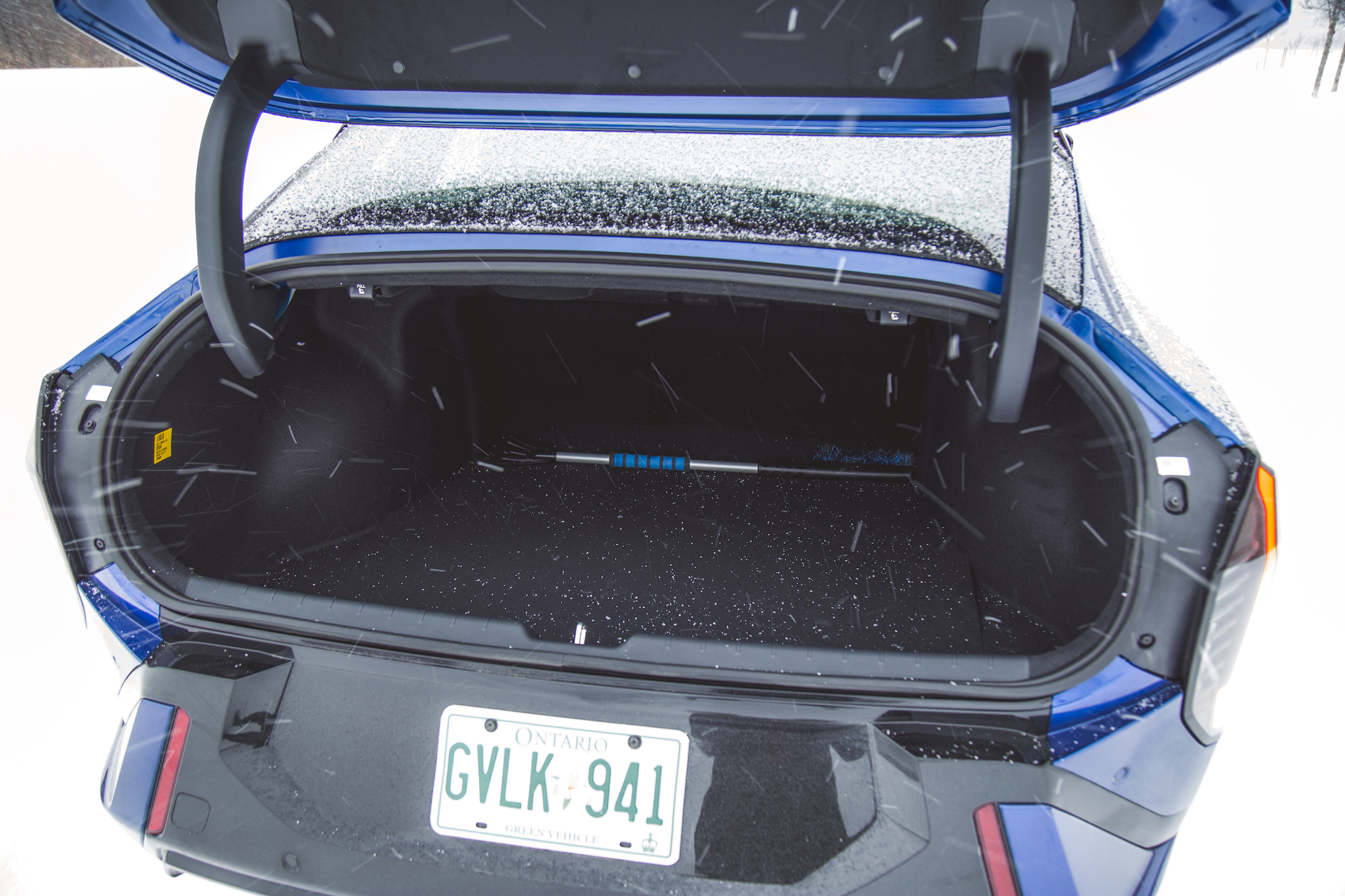 Maletero abierto de un coche azul en un entorno nevado, mostrando un interior espacioso y una matrícula con el número GVLK-941.