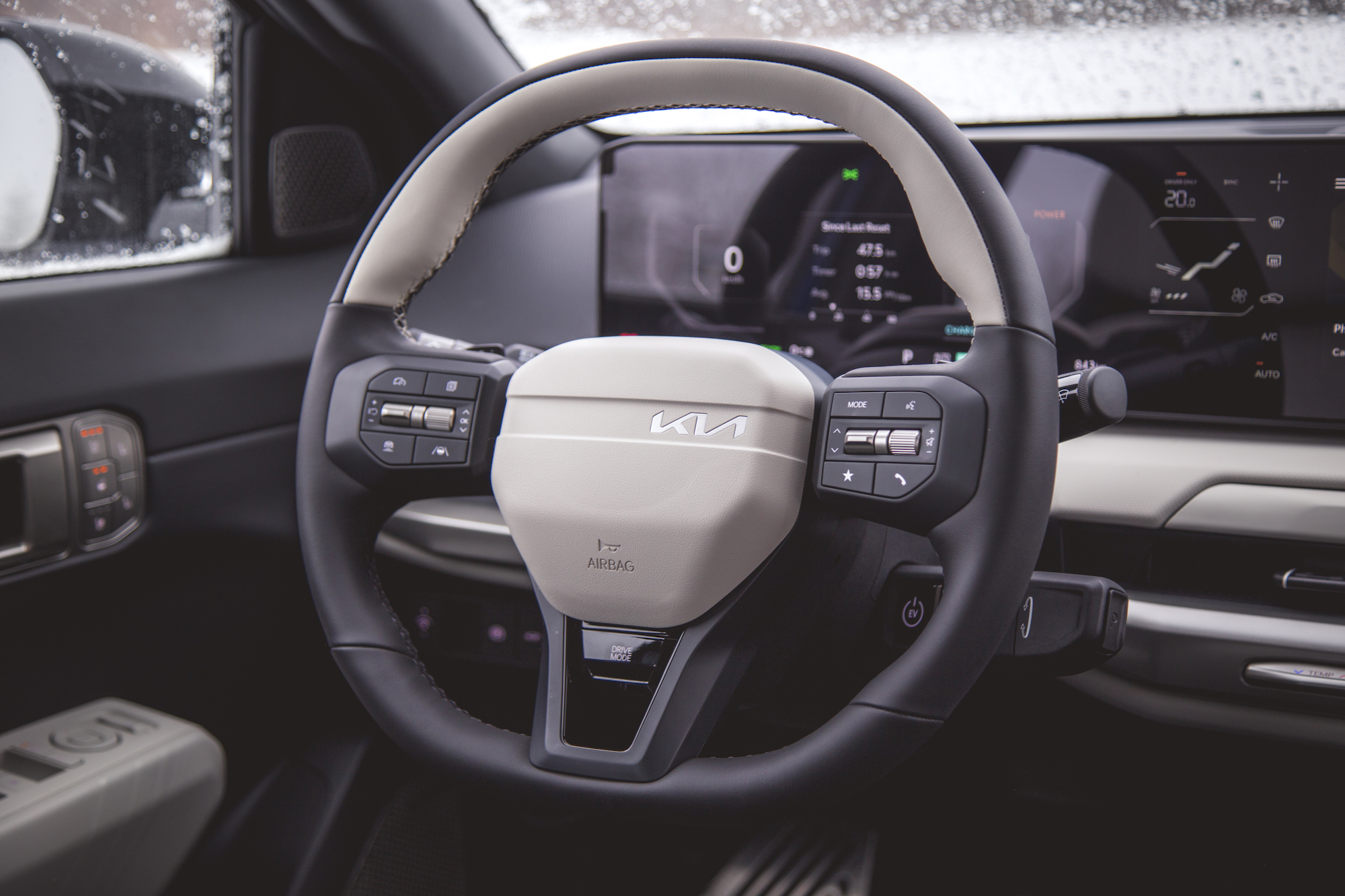 Vista cercana de un volante Kia con pantalla de tablero digital al fondo, que muestra botones de control y características de diseño moderno.