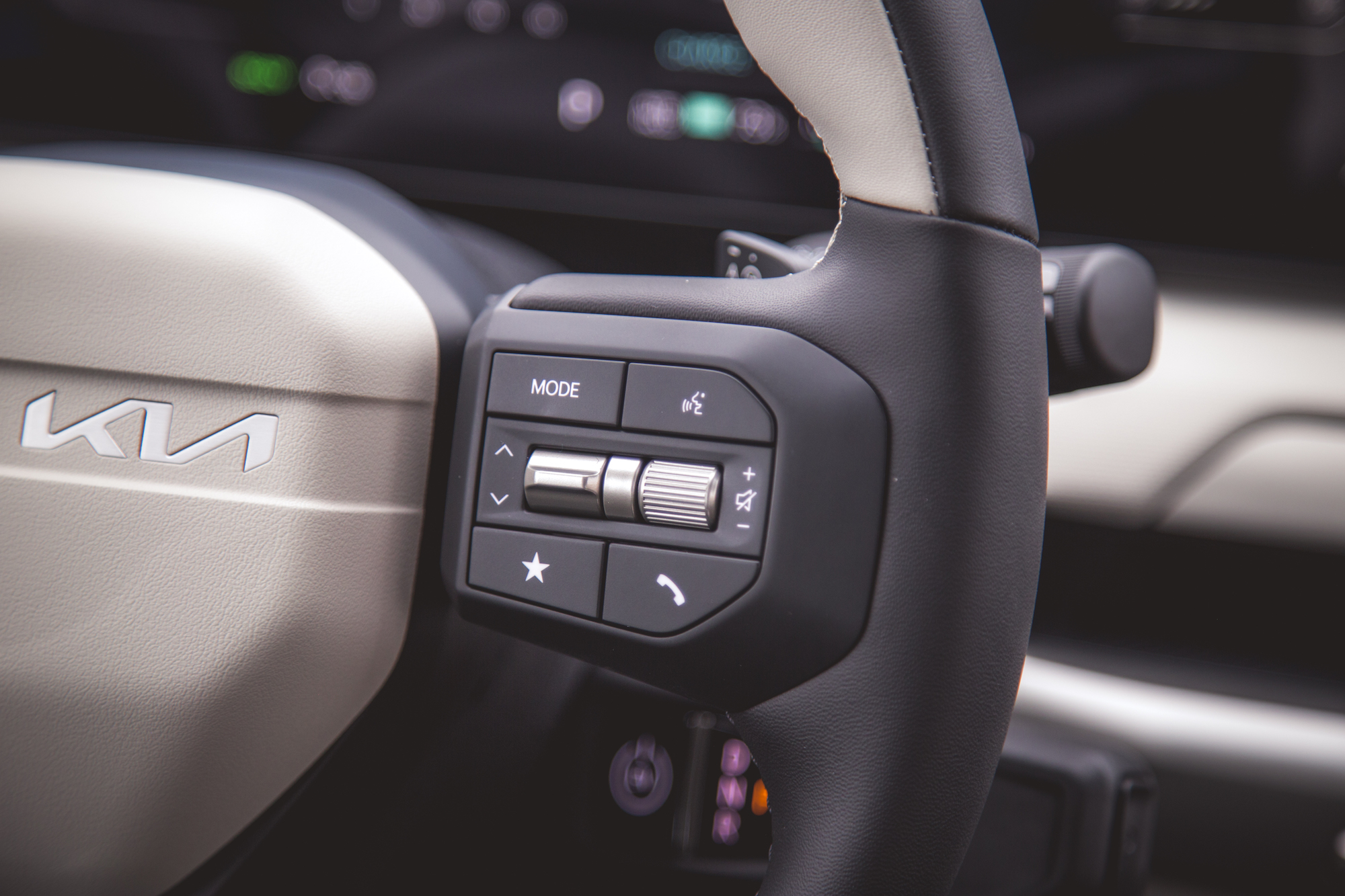 Primer plano de un volante en un vehículo Kia, resaltando los botones de control, incluidos el modo, el volumen y las opciones del teléfono.