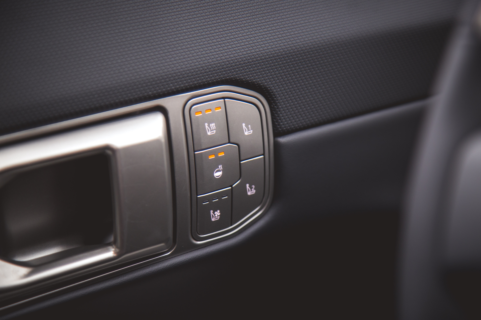 Primer plano de los controles de ajuste del asiento del automóvil con íconos iluminados para calefacción y reclinación.