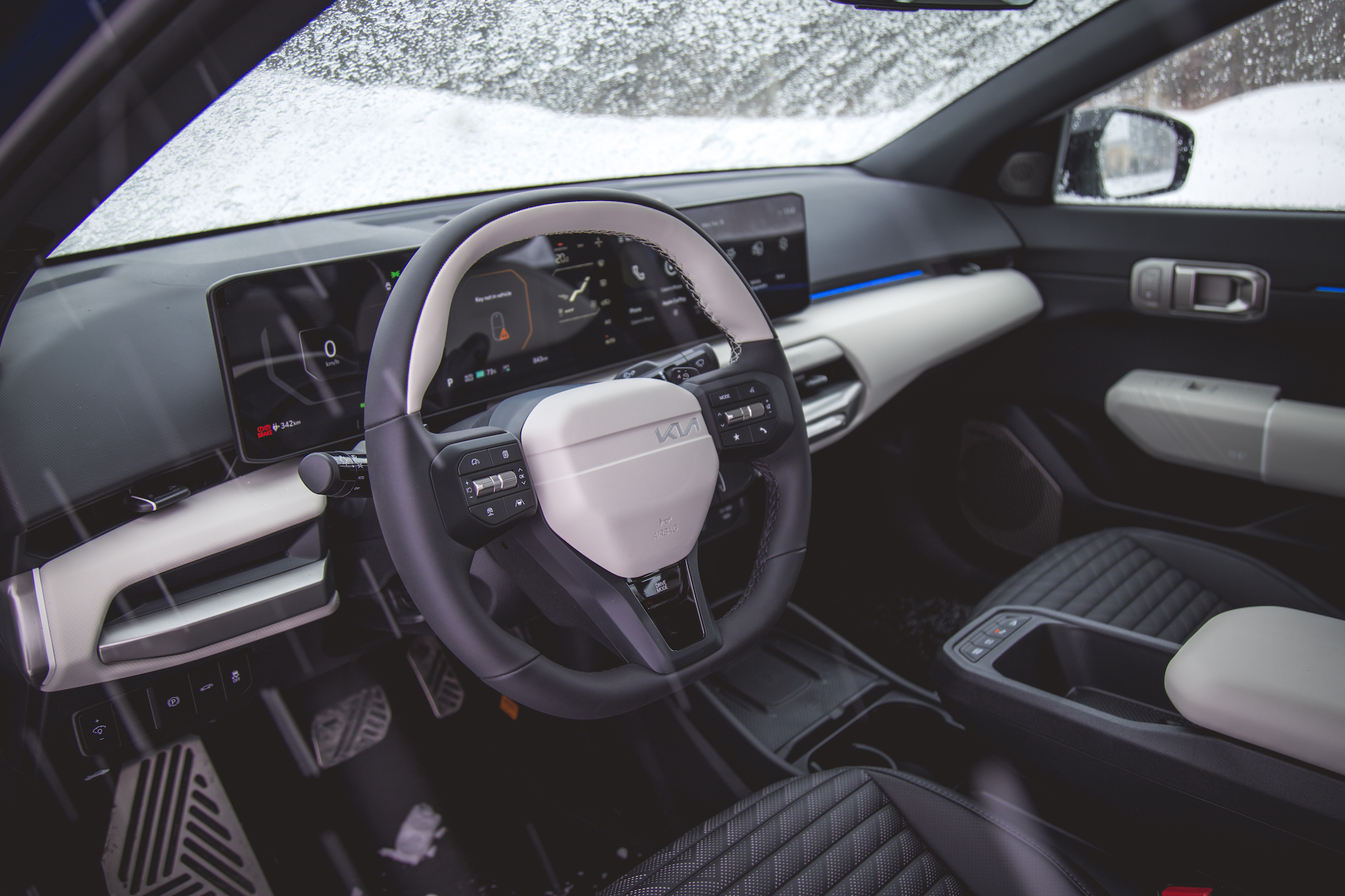 Vista interior de un coche Kia, que muestra el volante, la pantalla del salpicadero y los asientos de diseño moderno, rodeados de cristales cubiertos de nieve.