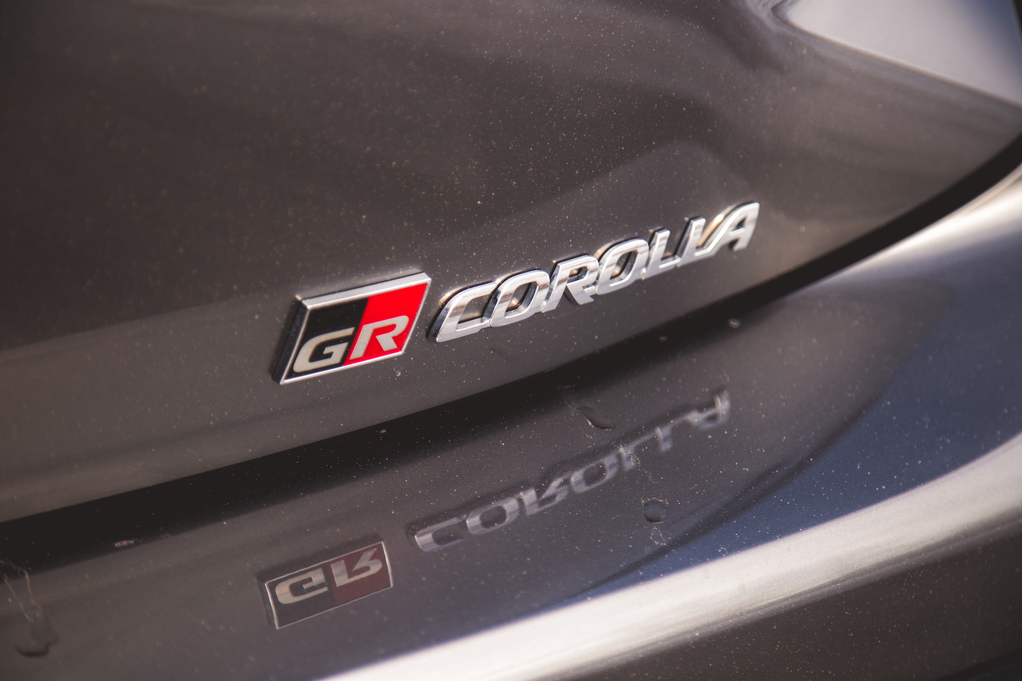 Primer plano de una insignia GR Corolla en el maletero de un automóvil, que muestra letras plateadas brillantes sobre un fondo oscuro.