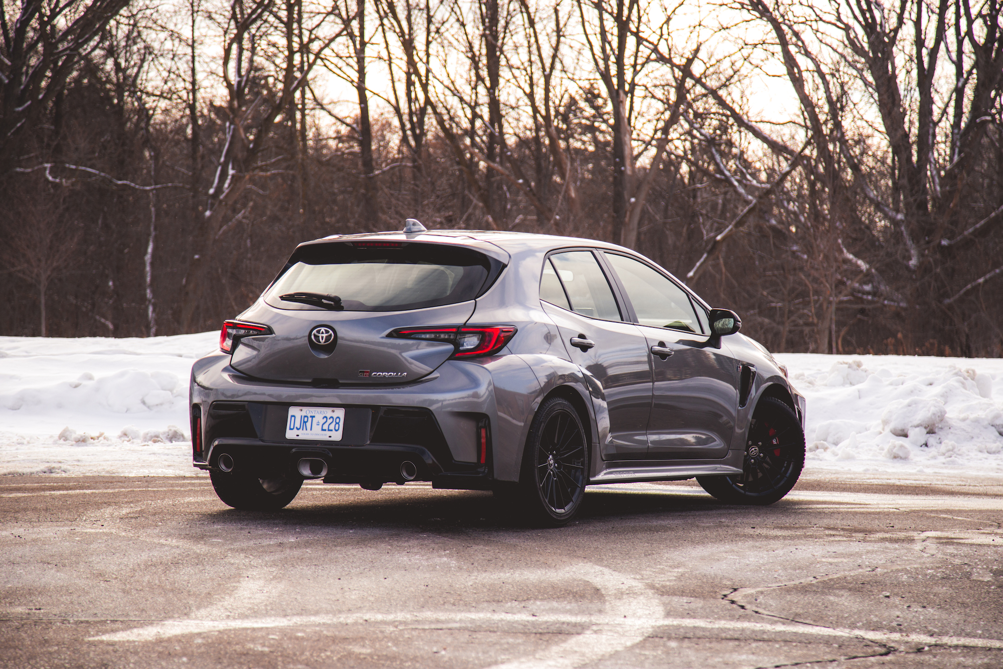 Un Toyota Corolla hatchback gris estacionado sobre una superficie nevada, mostrando su vista trasera con árboles al fondo.