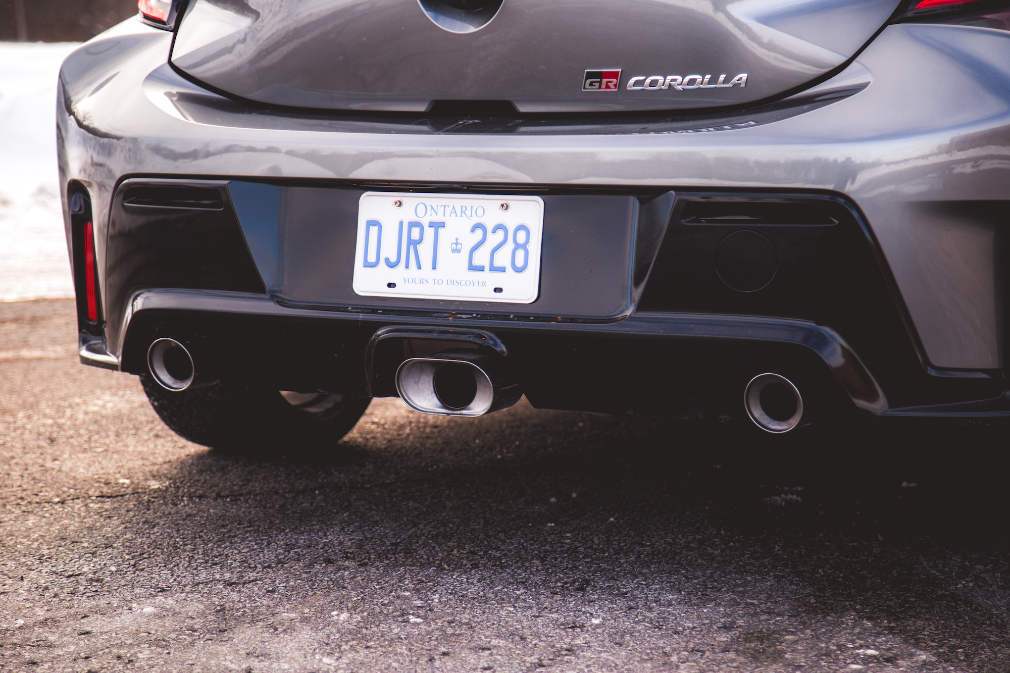 Vista cercana de la parte trasera de un Toyota GR Corolla gris, que muestra dos tubos de escape y una matrícula de Ontario.