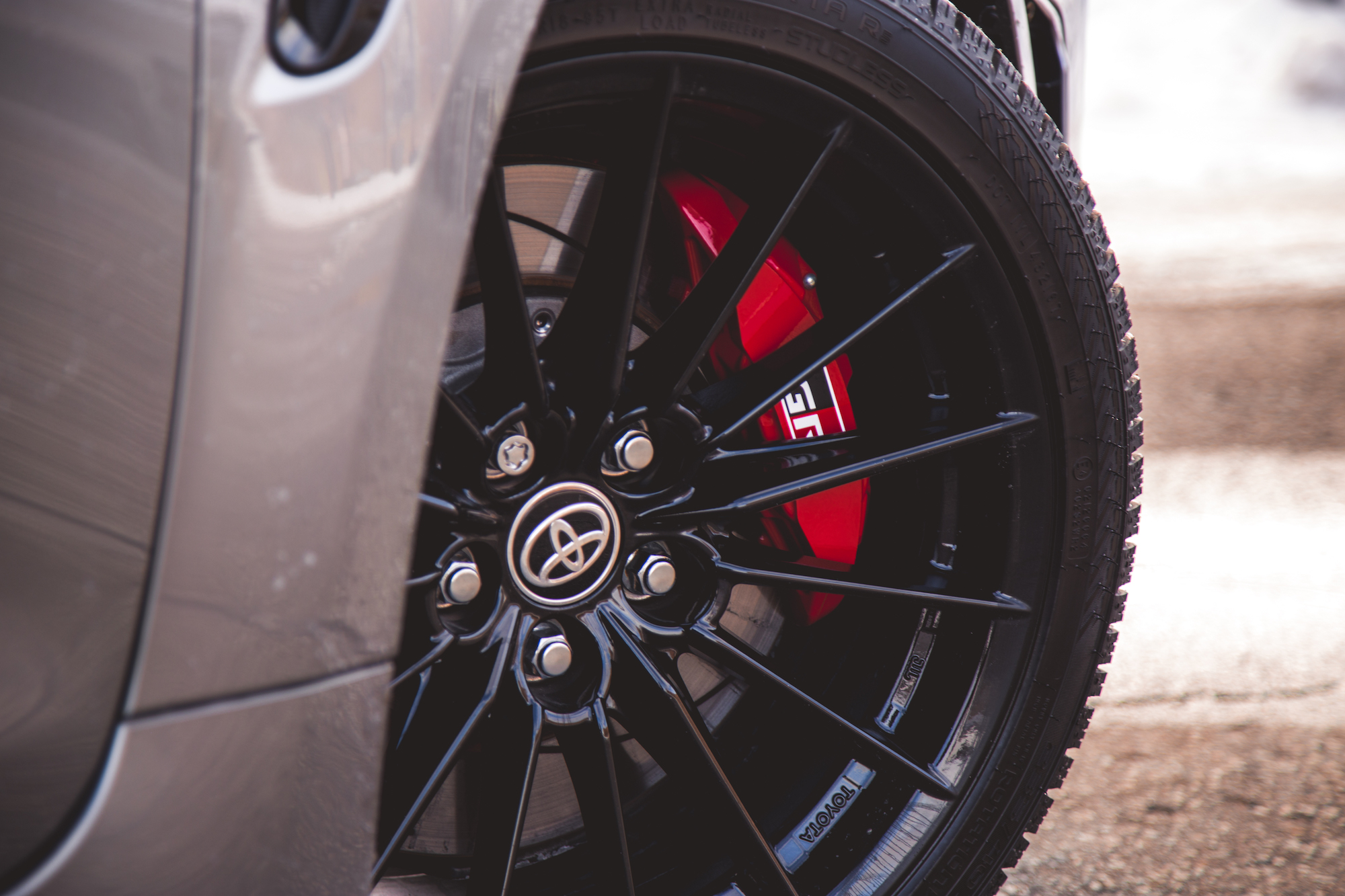 Primer plano de una llanta de aleación negra con un logotipo prominente de Toyota y pinzas de freno rojas, que muestra un neumático de alto rendimiento.