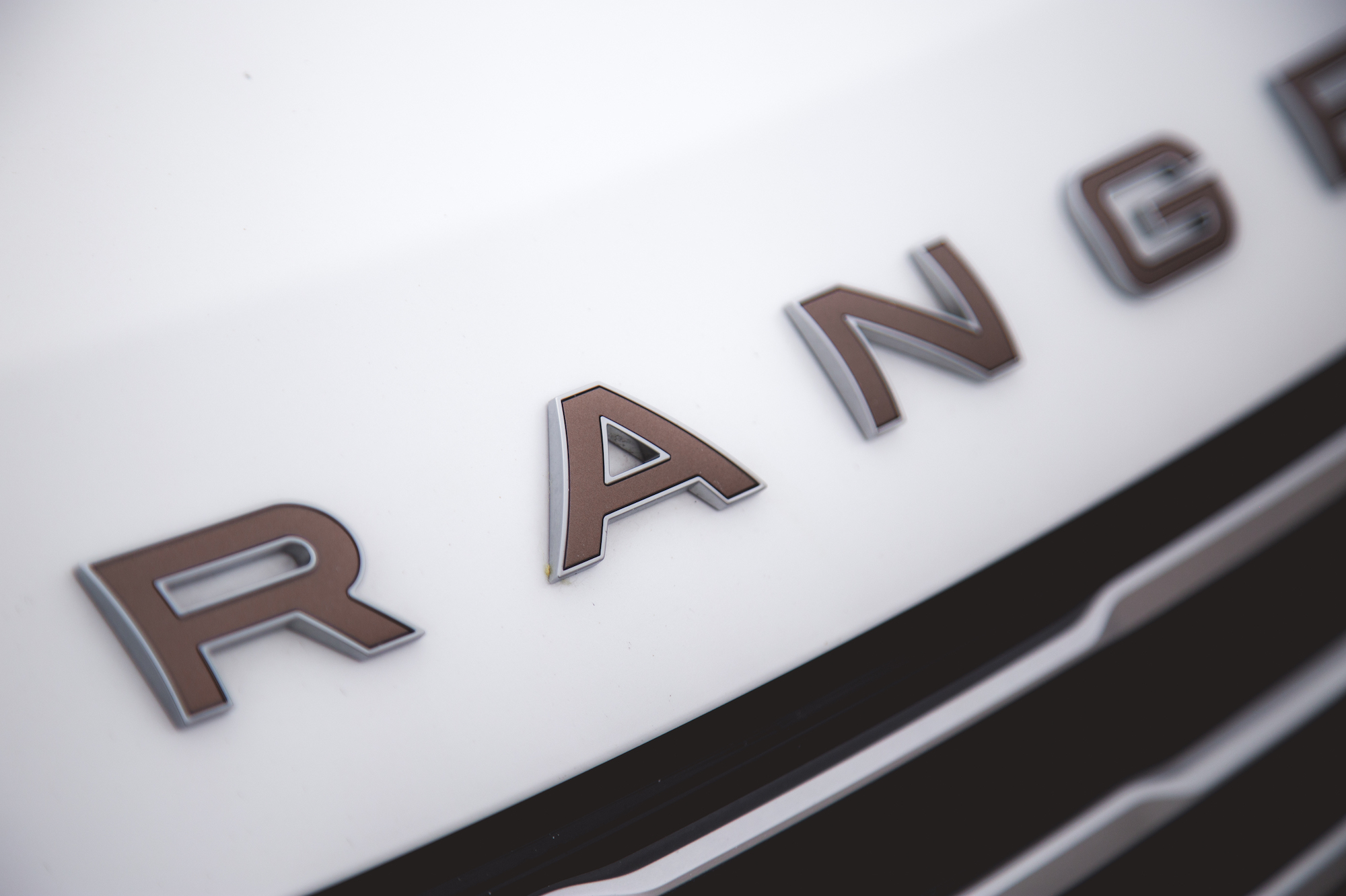 Primer plano del logotipo 'RANGER' en la parrilla delantera de un vehículo blanco.