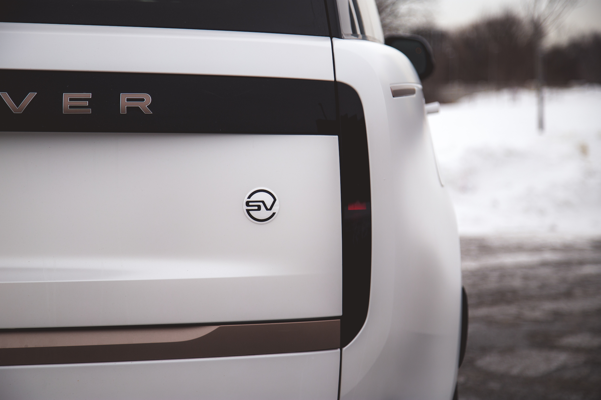 Primer plano de la parte trasera de un vehículo blanco que muestra el nombre 'Rover' y un emblema con las iniciales 'SV'.