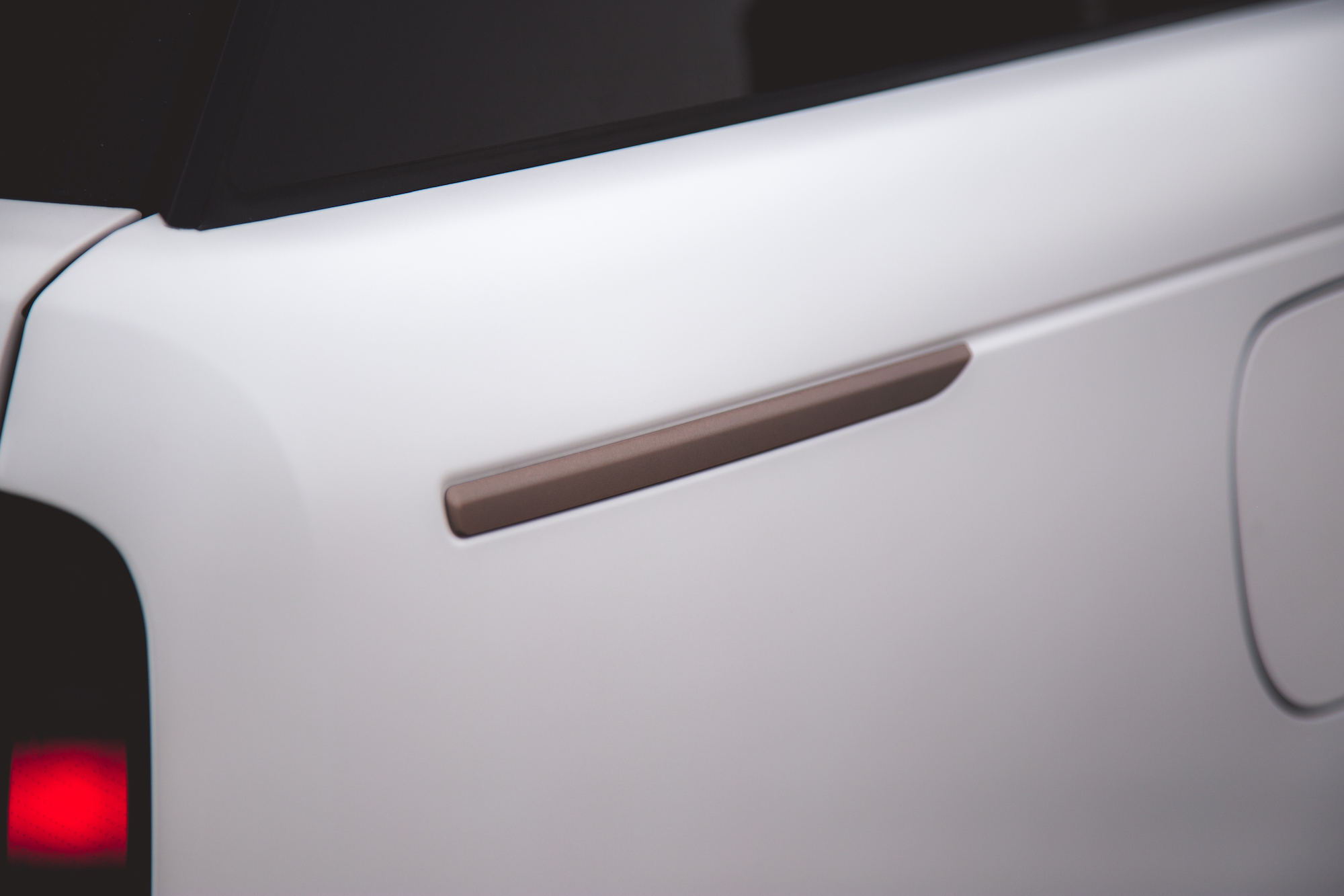 Primer plano de la puerta trasera de un automóvil blanco con una sutil manija marrón.