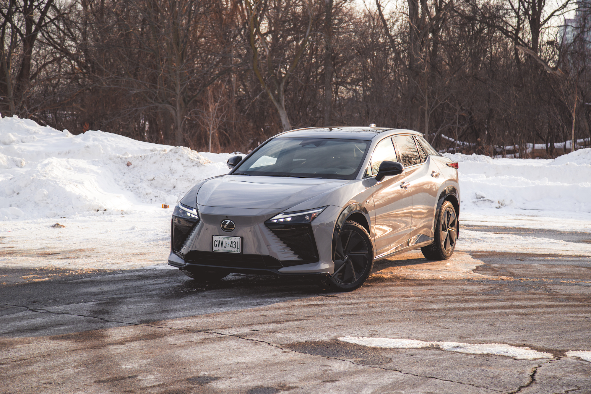 A modern gray SUV parked on a snowy surface, surrounded by trees in the background.