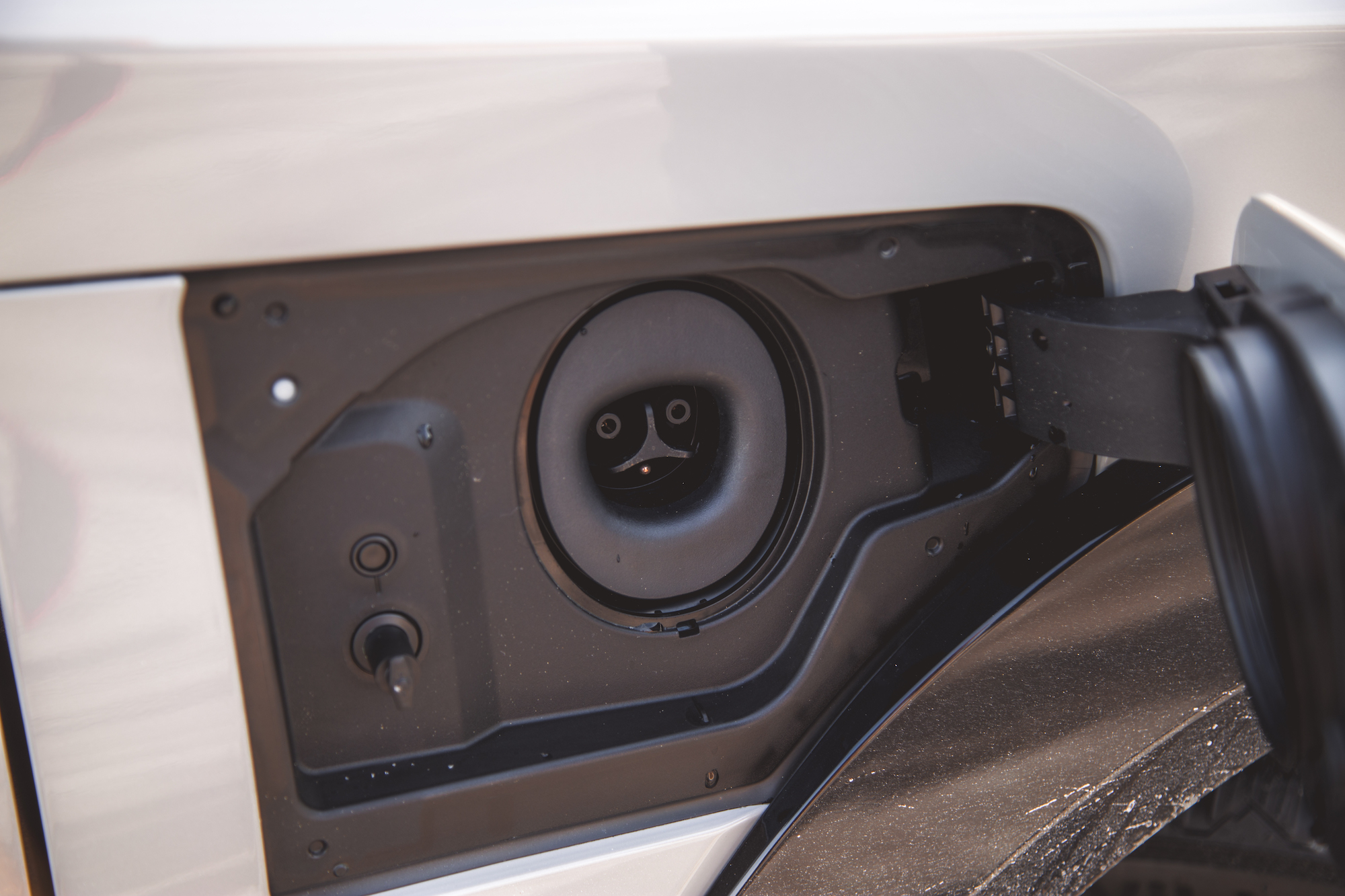 Close-up of an electric vehicle charging port, showing the charging connector and surrounding panel details.