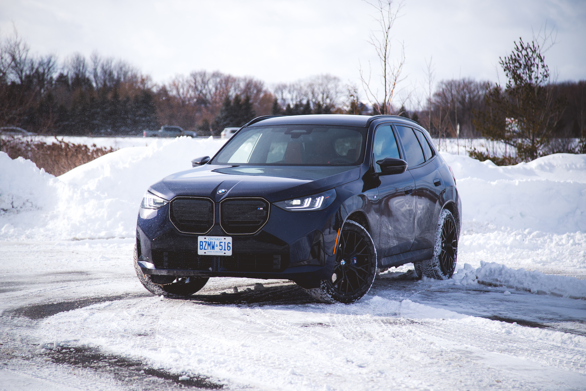 Black BMW SUV parked on snow-covered ground with trees in the background.