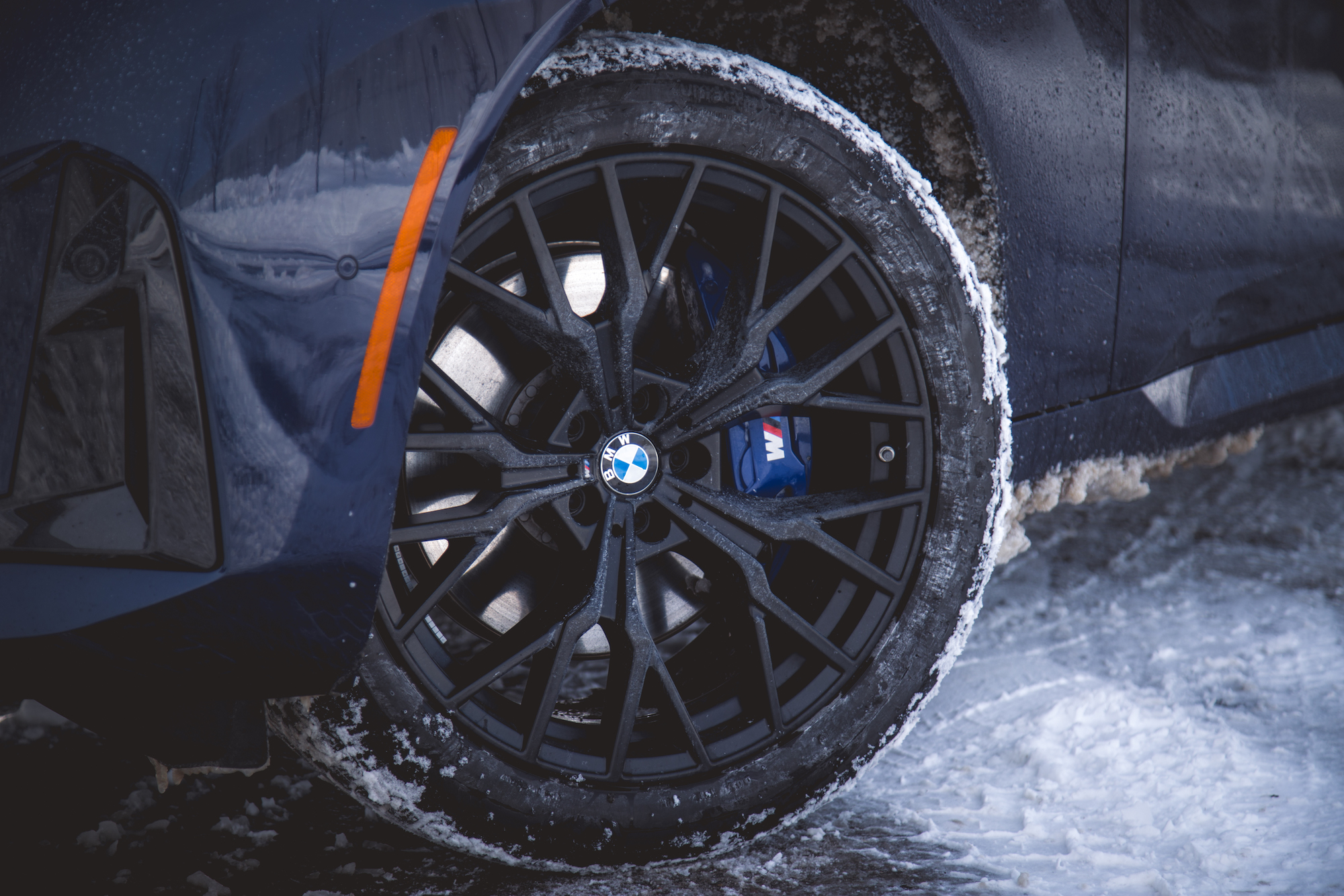 Close-up of a black BMW wheel with a snow-covered tire and brake caliper, set against a snowy background.