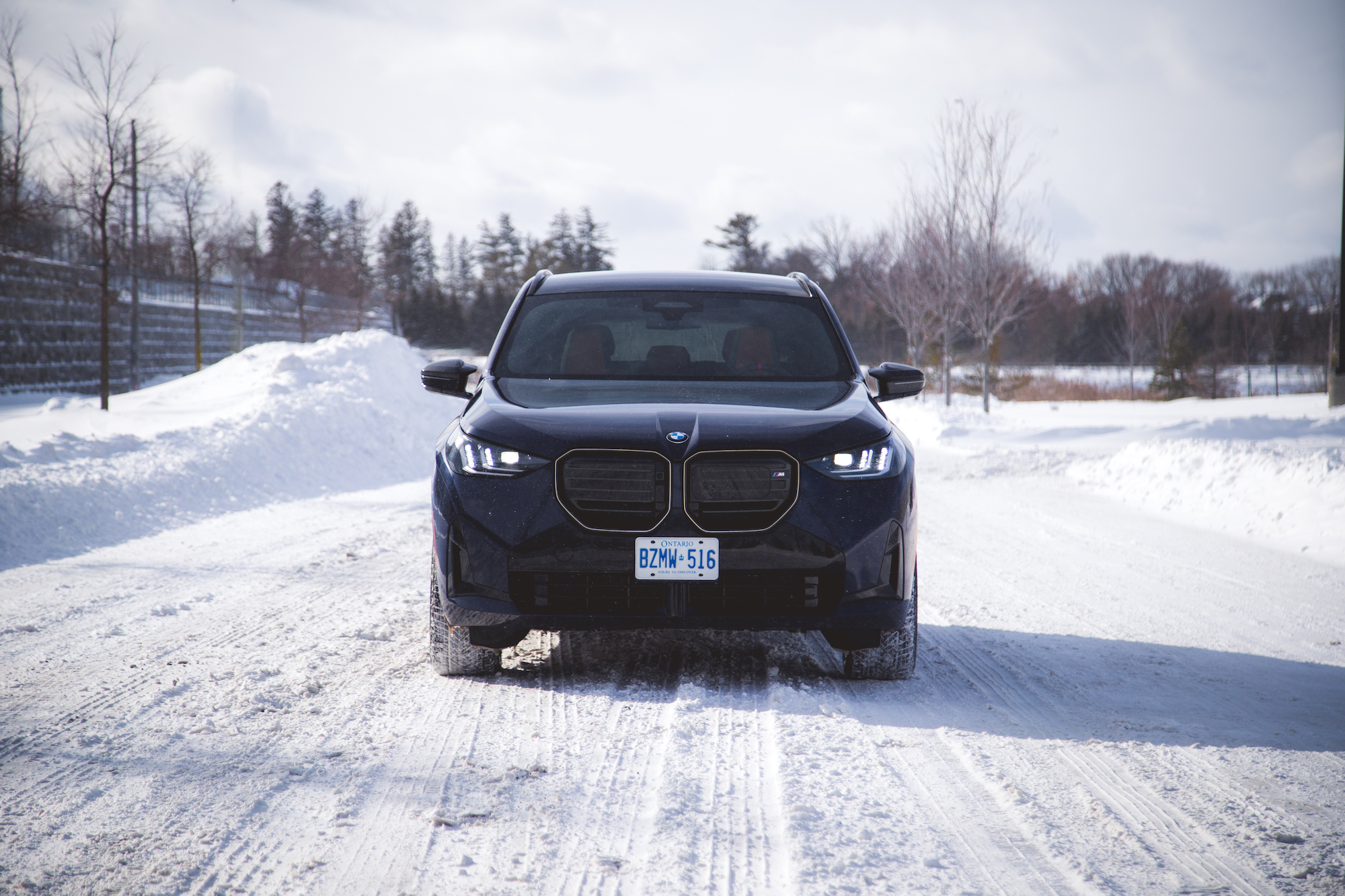 A black BMW SUV parked on a snowy road with trees in the background.