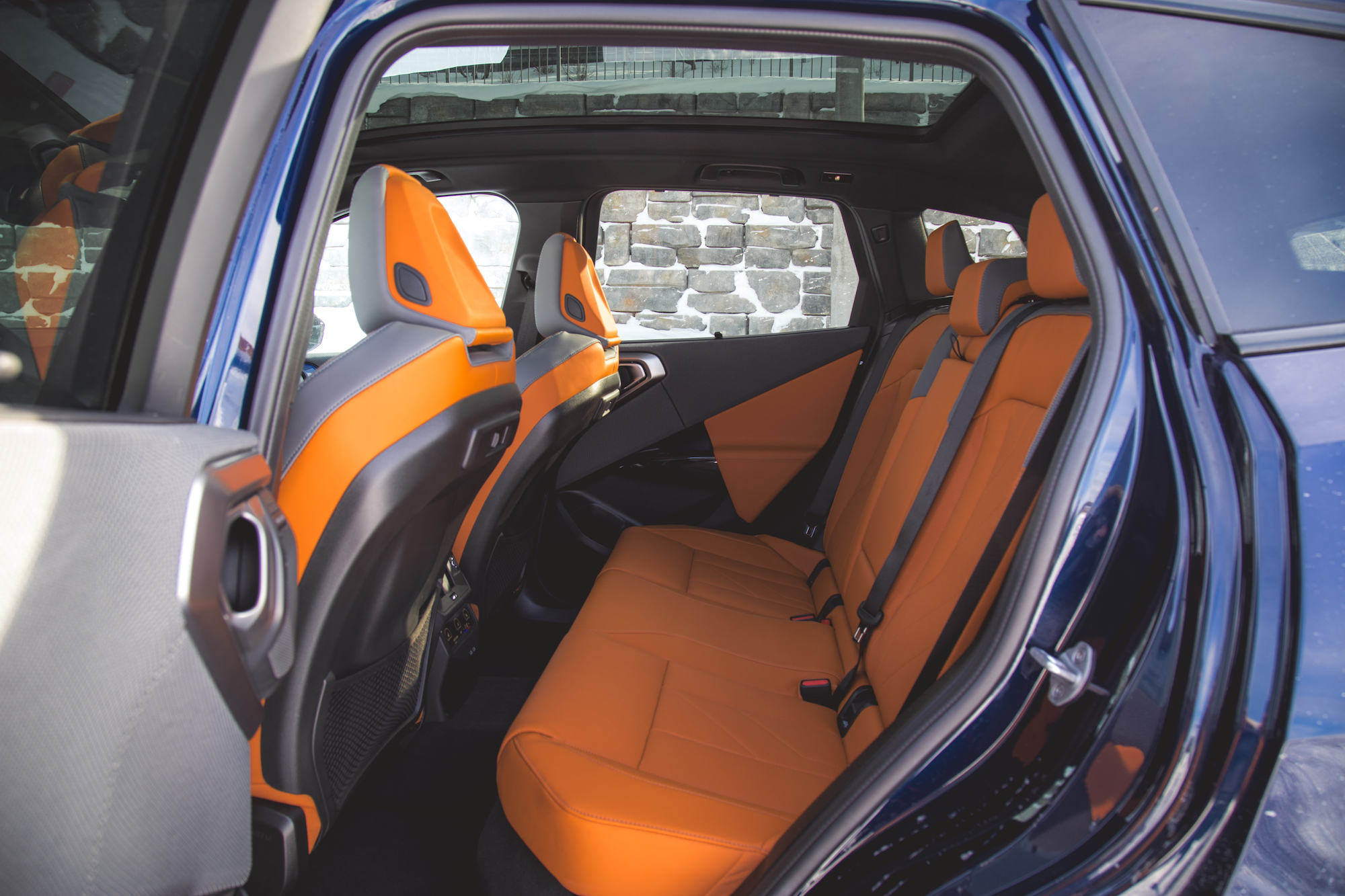 Interior view of a car's backseat featuring orange and gray seating, with a scenic stone wall visible through the windows.