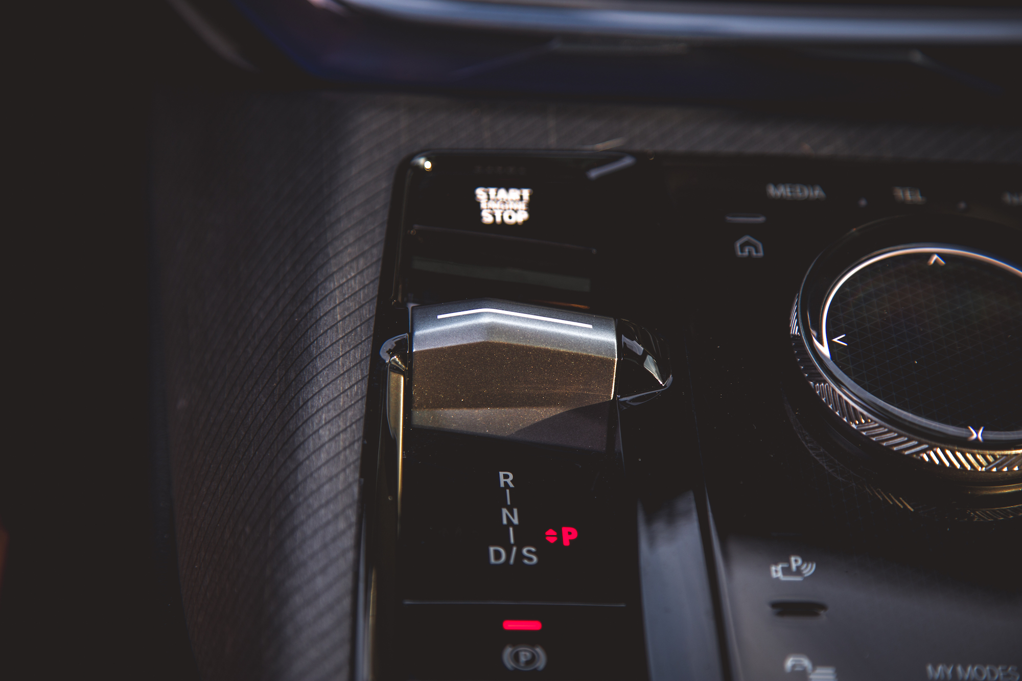 Close-up of a car's gear shift with markings for R, N, D, S, and P, alongside a start-stop button and other controls.