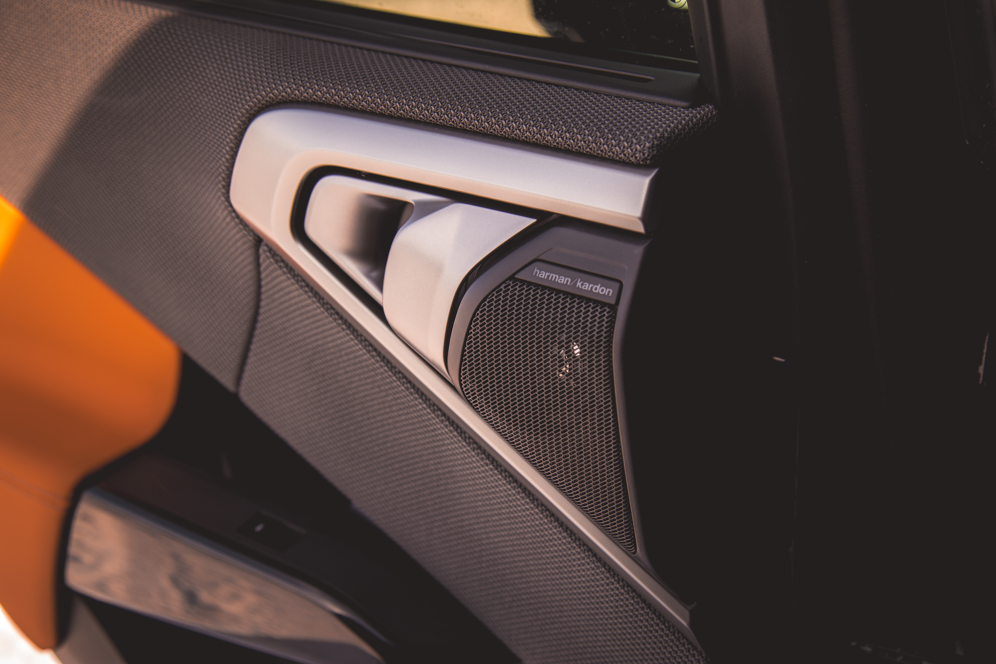 Close-up of a car door interior featuring a Harman Kardon speaker and modern door handle design.