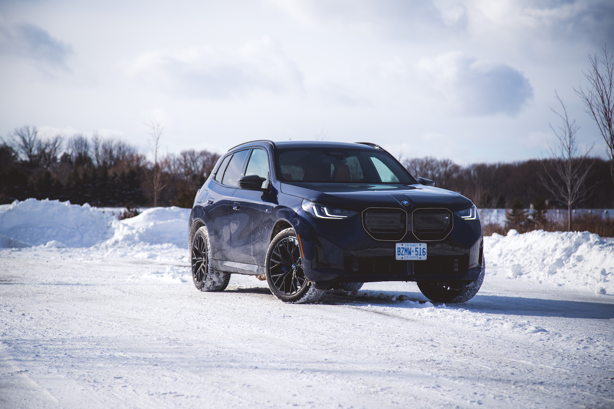 A dark blue BMW SUV parked on snow-covered ground with a winter landscape in the background.