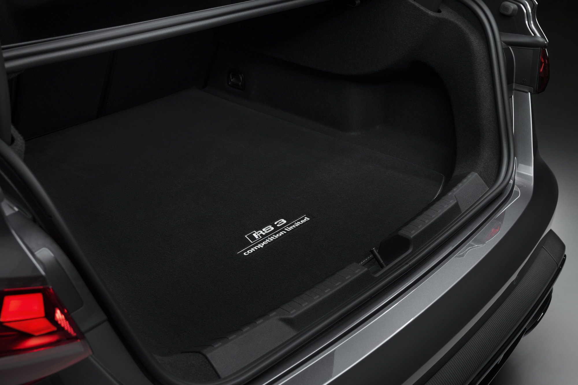 Close-up view of the trunk space in a car, featuring a black carpeted floor with an 'RS 3 competition limited' badge.