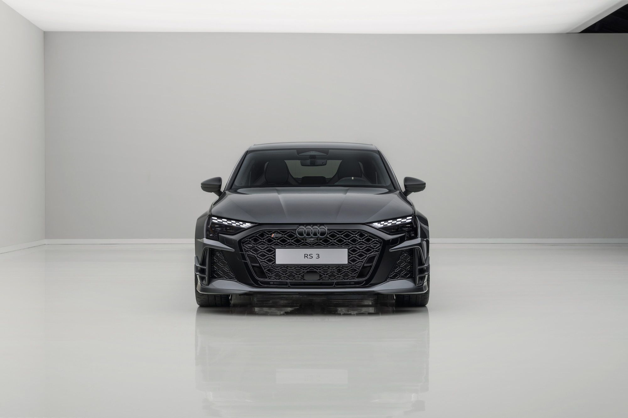 Front view of a black Audi RS 3 against a minimalist light gray background.