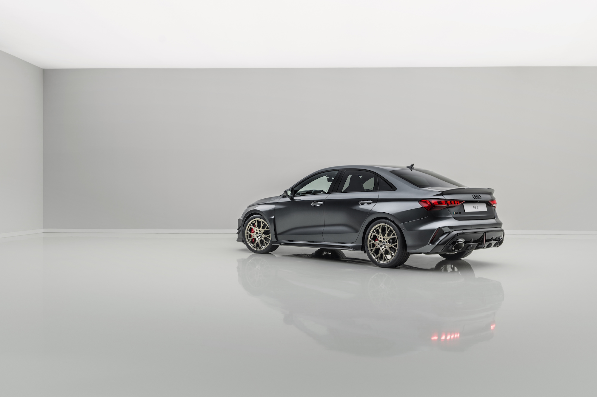 A sleek, dark gray sports sedan with distinctive wheels and a modern design, showcased in a minimalist studio setting.
