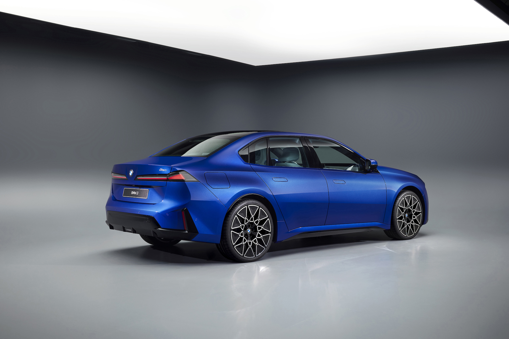 A blue BMW sedan viewed from the rear in a studio setting, showcasing its modern design and sleek lines.